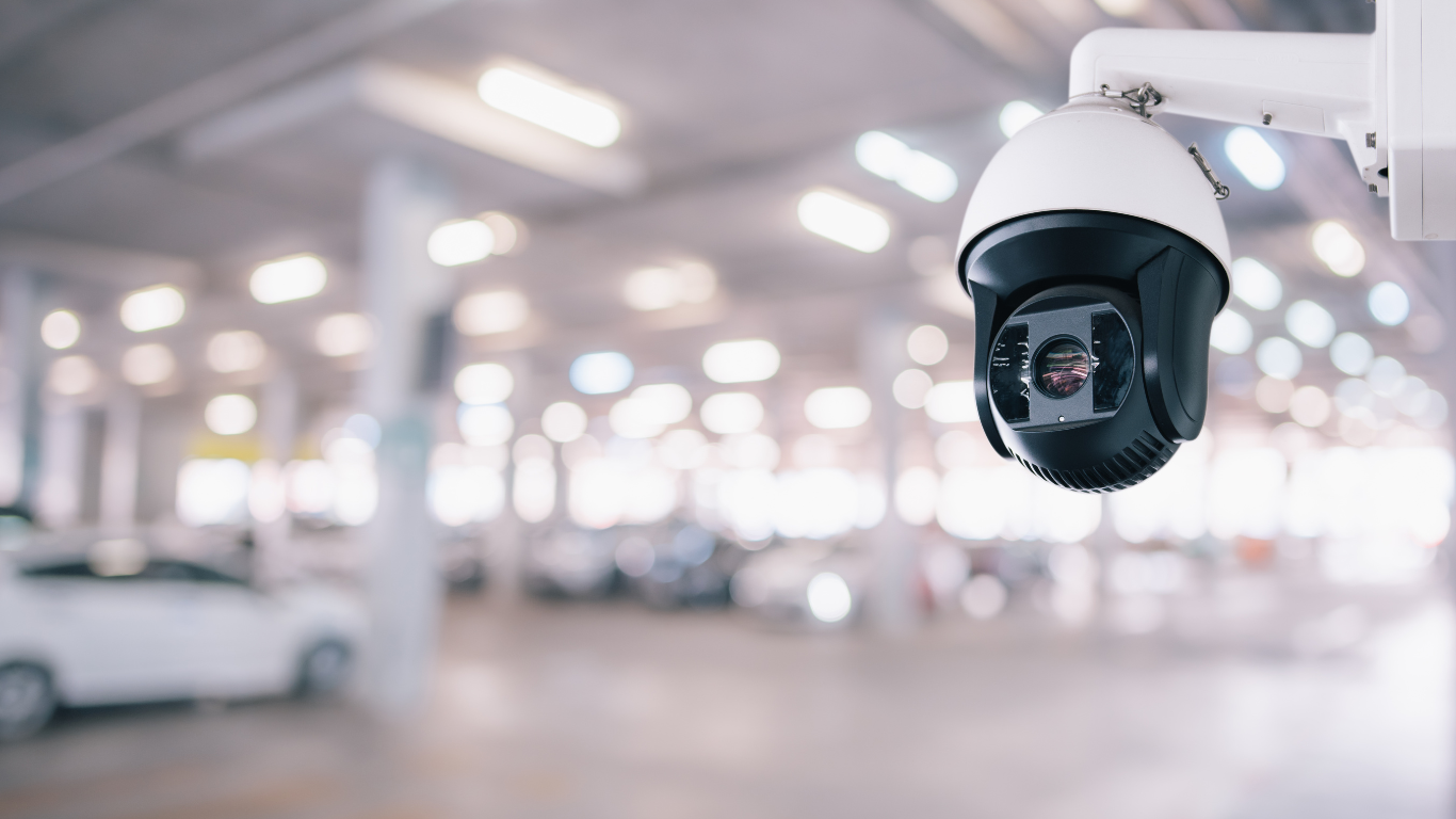 A security camera is hanging from the side of a building in a parking garage.