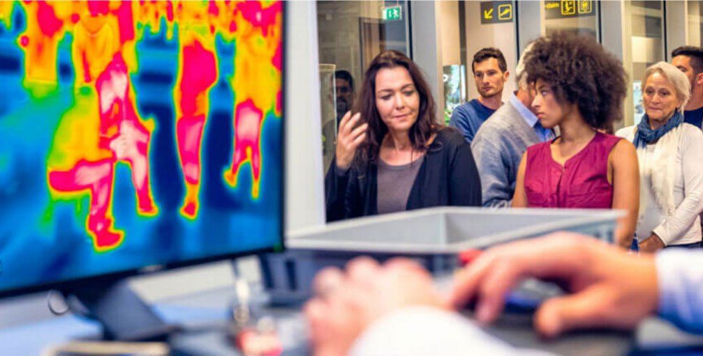 A group of people are standing in front of a computer screen.