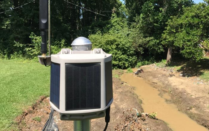A solar powered device is sitting next to a muddy stream.