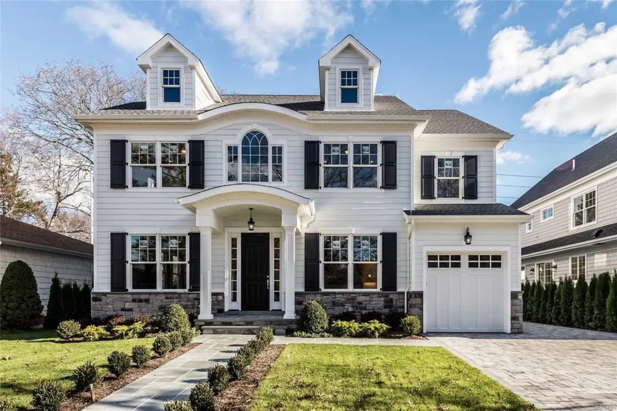 A large white house with black shutters is for sale.