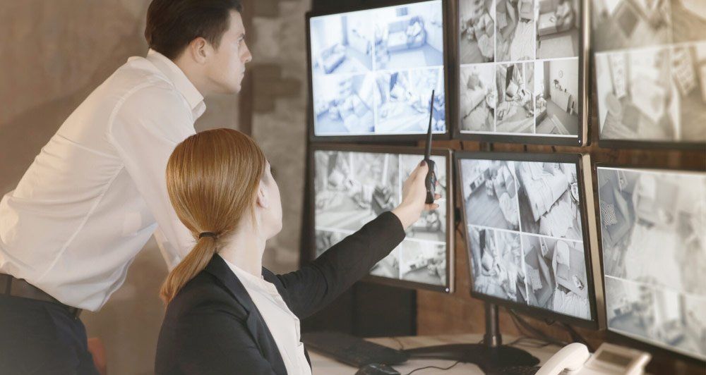 A man and a woman are looking at a bunch of monitors.