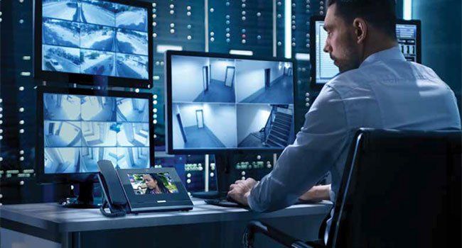 A man is sitting at a desk in front of a bunch of monitors.