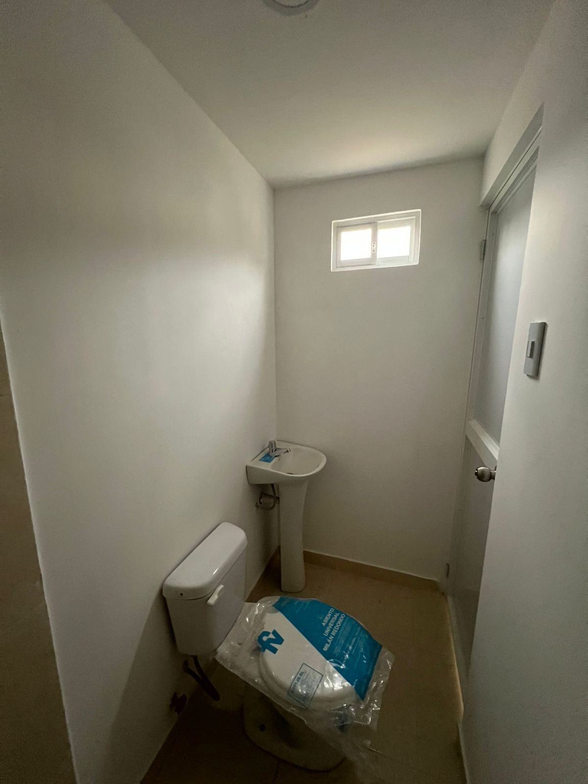 Un baño pequeño y minimalista con paredes blancas, un lavabo de pedestal