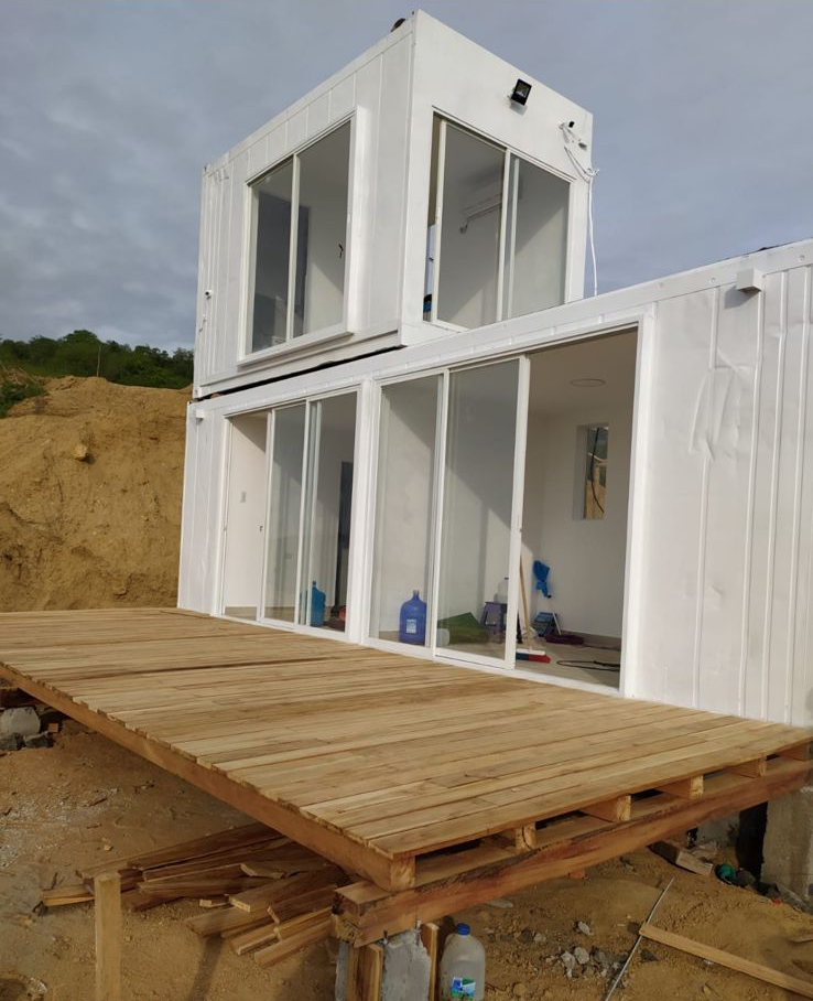 Una moderna casa modular blanca de dos plantas con puertas correderas de cristal y una terraza de madera