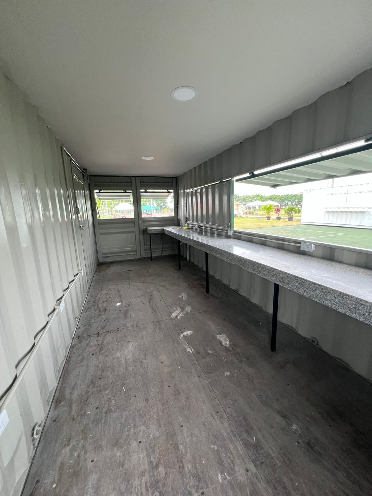 Un contenedor de transporte reconvertido, largo y estrecho, con techo blanco, paredes grises