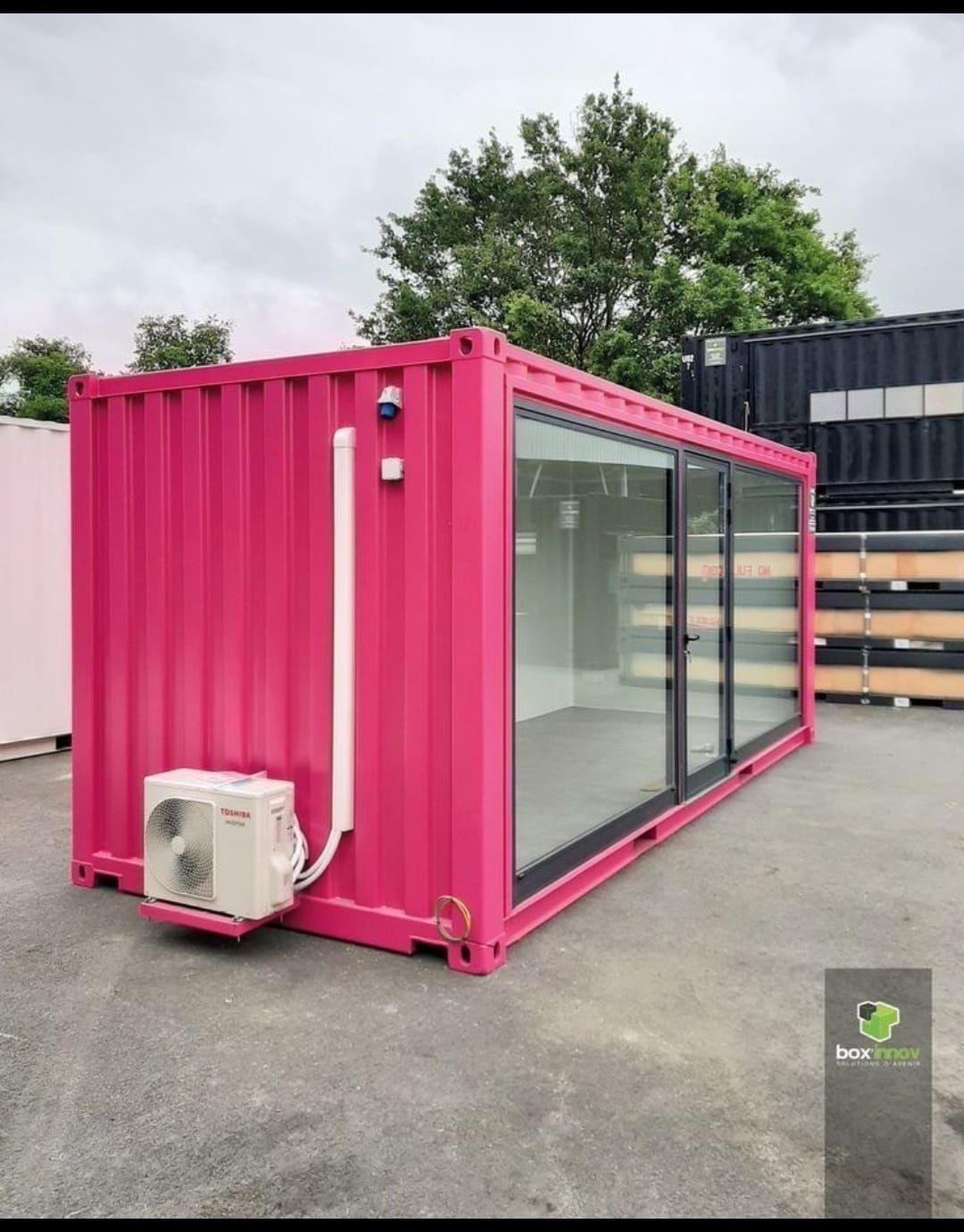 Un contenedor de transporte de color rosa vibrante reconvertido en oficina, con grandes puertas correderas de cristal