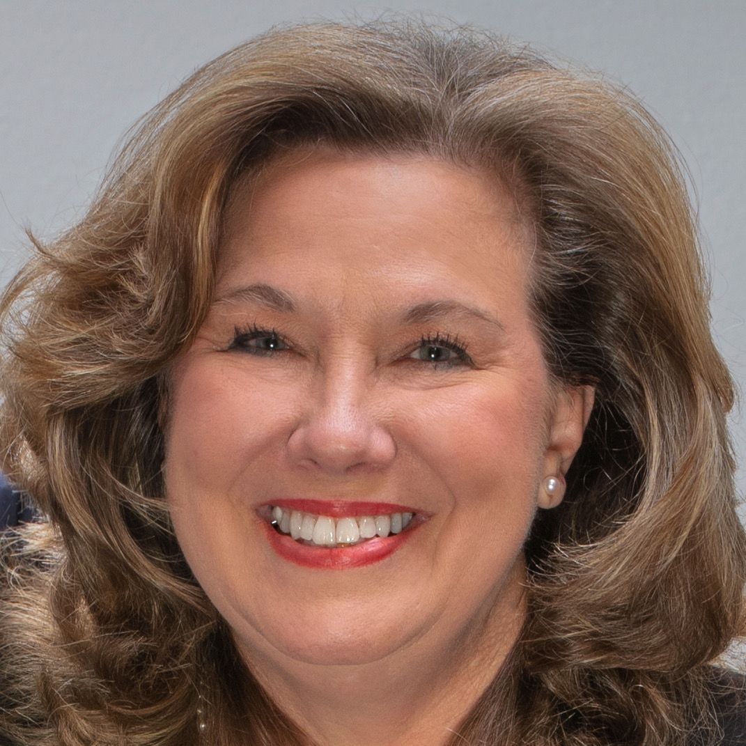 Amanda Rogers at Amjet Aviation; Smiling woman with wavy brown hair wearing a dark jacket, pearl earrings, and red lipstick.