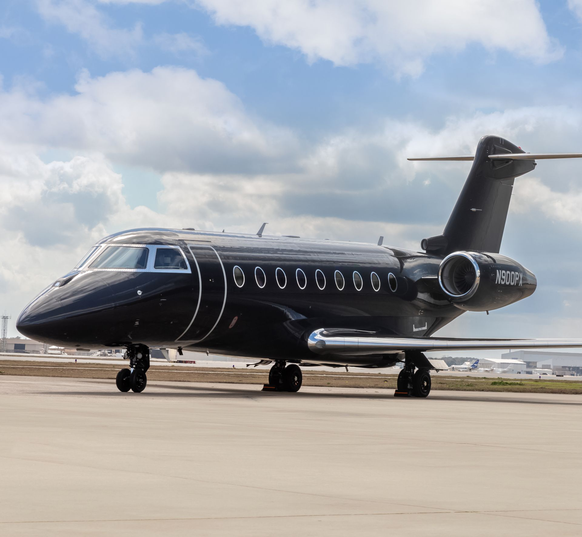Black Gulfstream G280 private jet on a tarmac, parked under a cloudy sky.