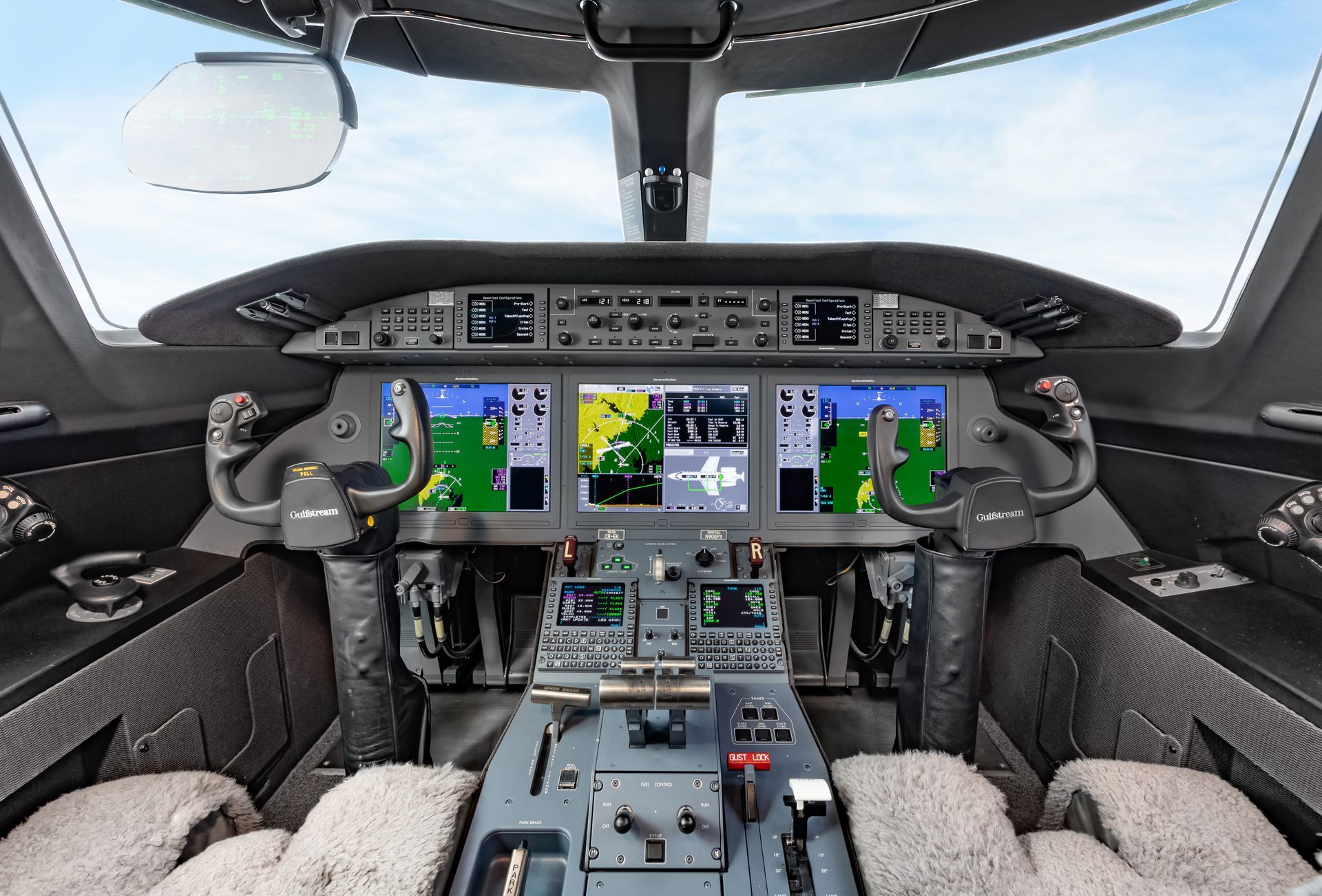 Airplane cockpit interior view with multiple display screens, controls, and pilot seats.