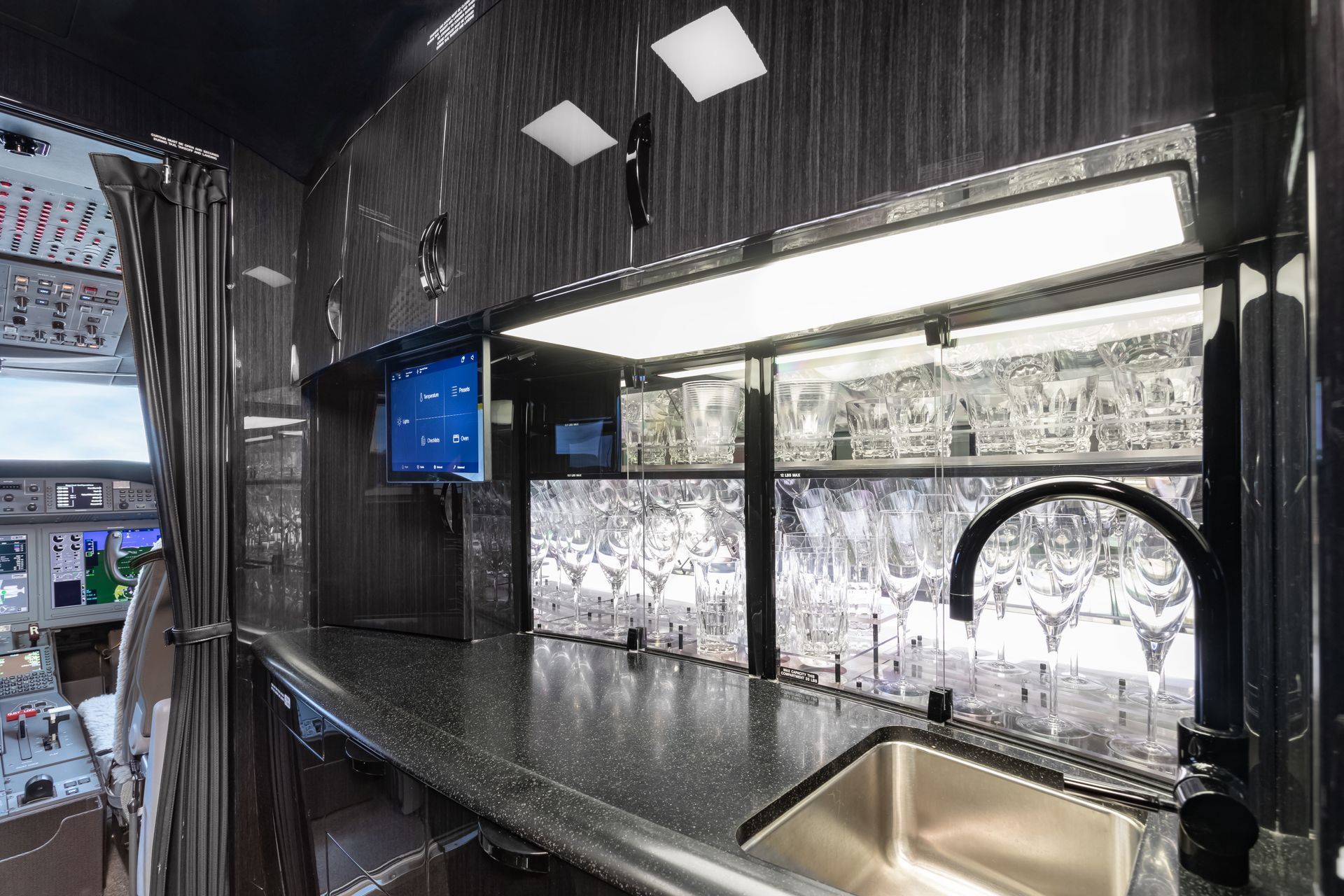 Interior view of a black airplane bar with a sink, TV, and countertop.