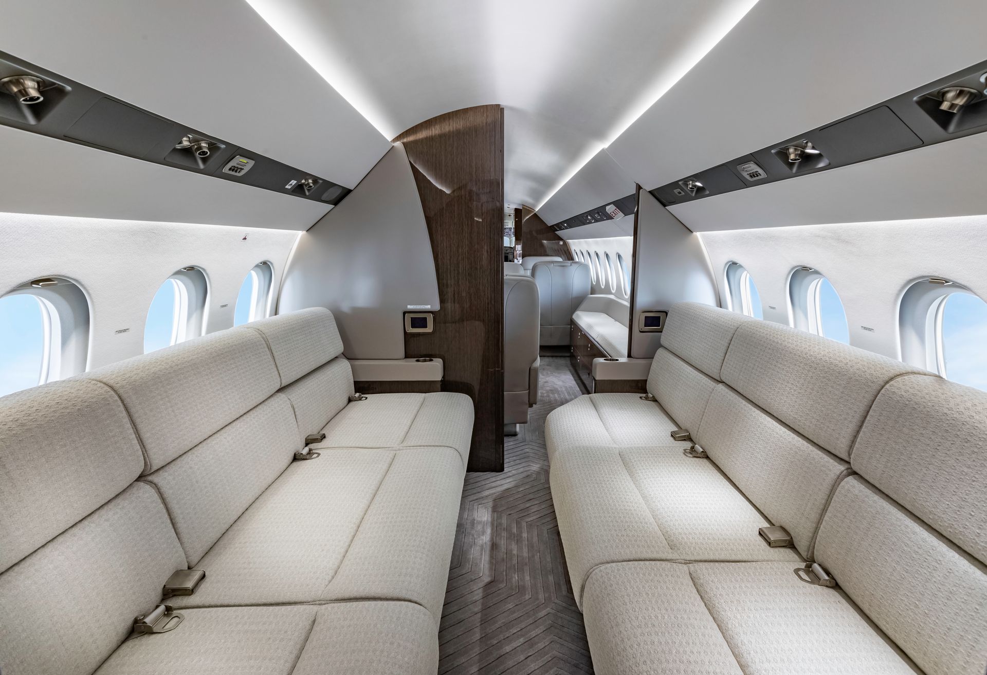 Interior of a private jet with cream-colored seating, wood paneling, and oval windows showing a blue sky.