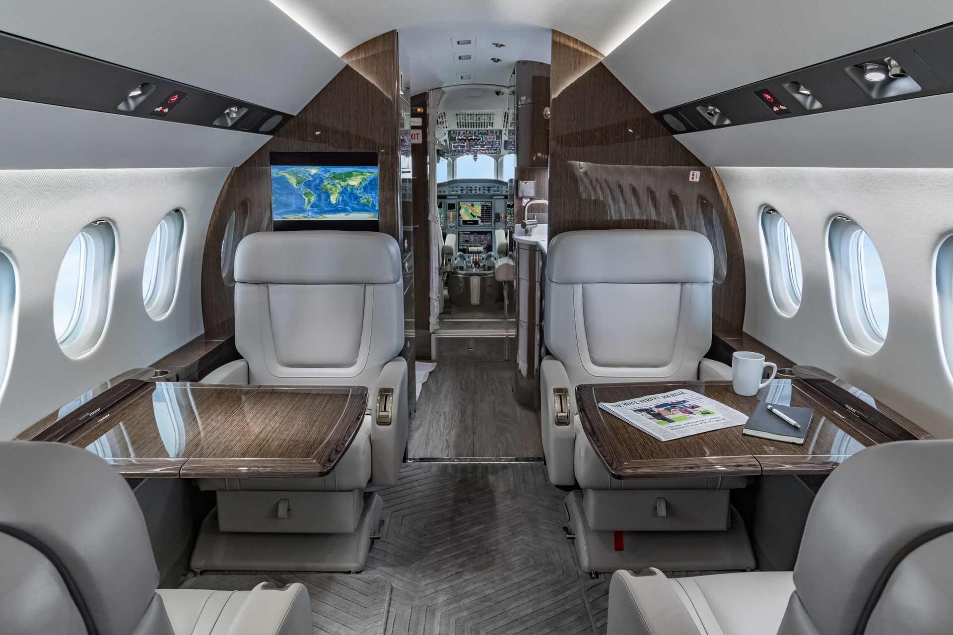 Interior of a luxury private jet with two plush white seats, tables, and a monitor.