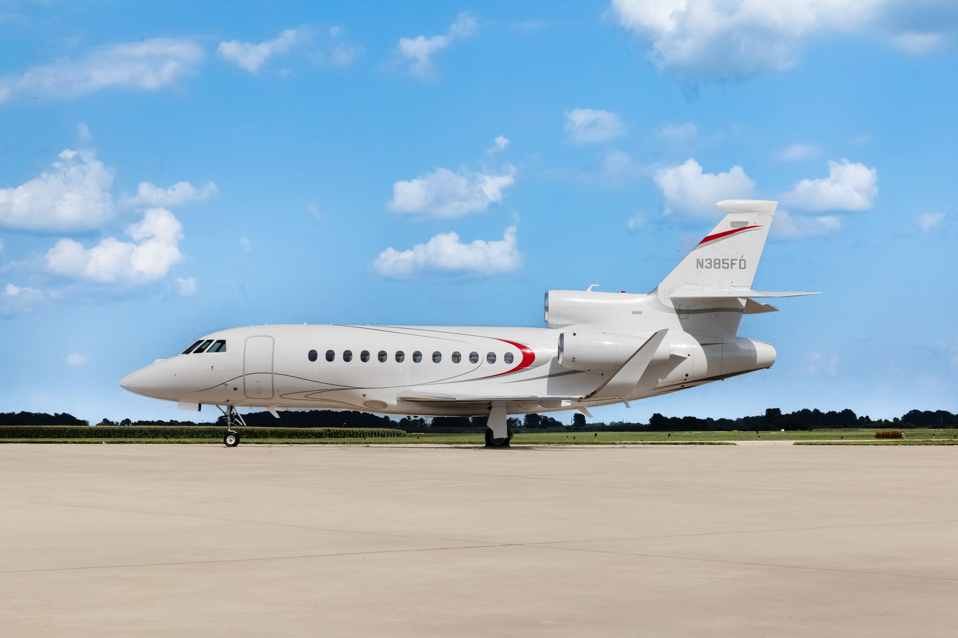 A Dassualt Falcon 900EXy, private jet on a tarmac under a blue sky with clouds.