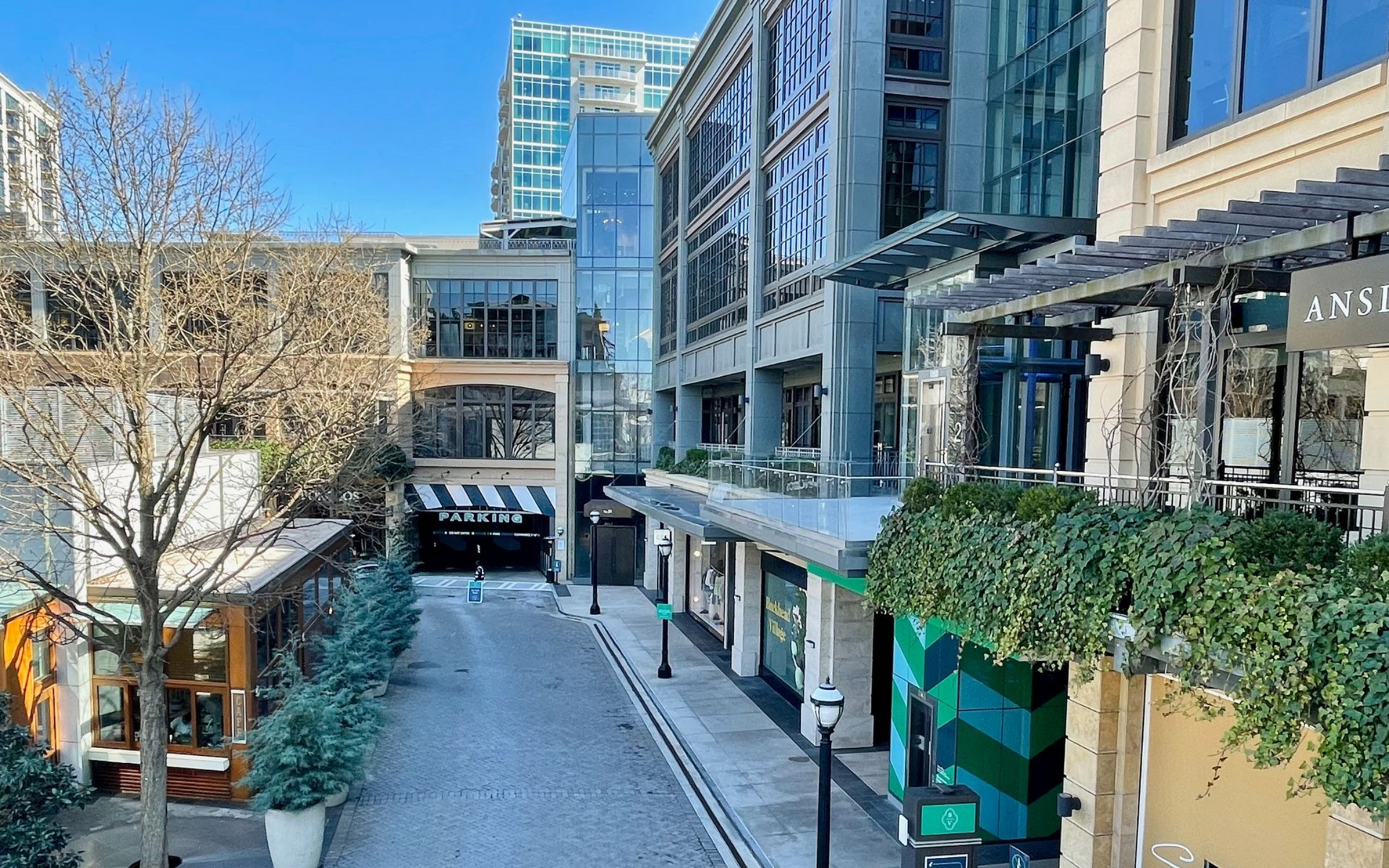 An upscale outdoor shopping street with storefronts, trees, and buildings under a bright sky, located in Buckhead Village District of Atlanta.