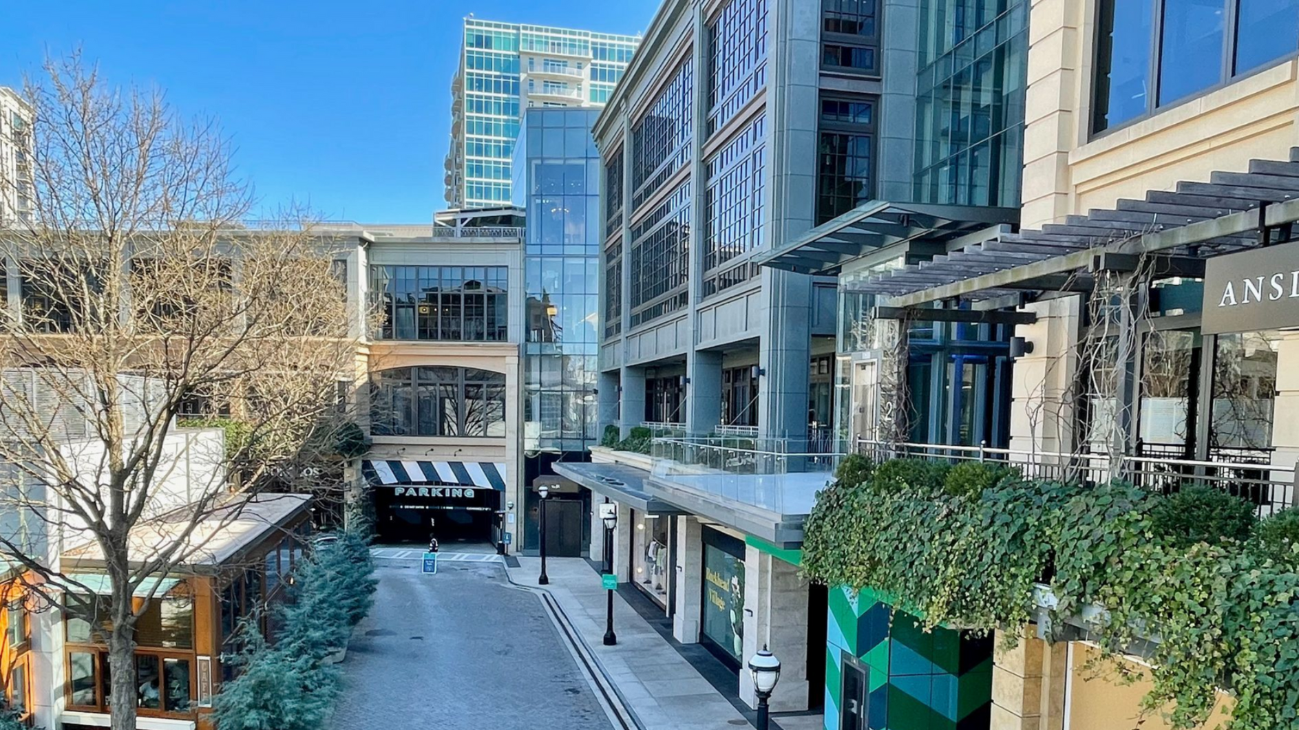 An urban outdoor scene with buildings, an open-air walkway, and lush greenery.