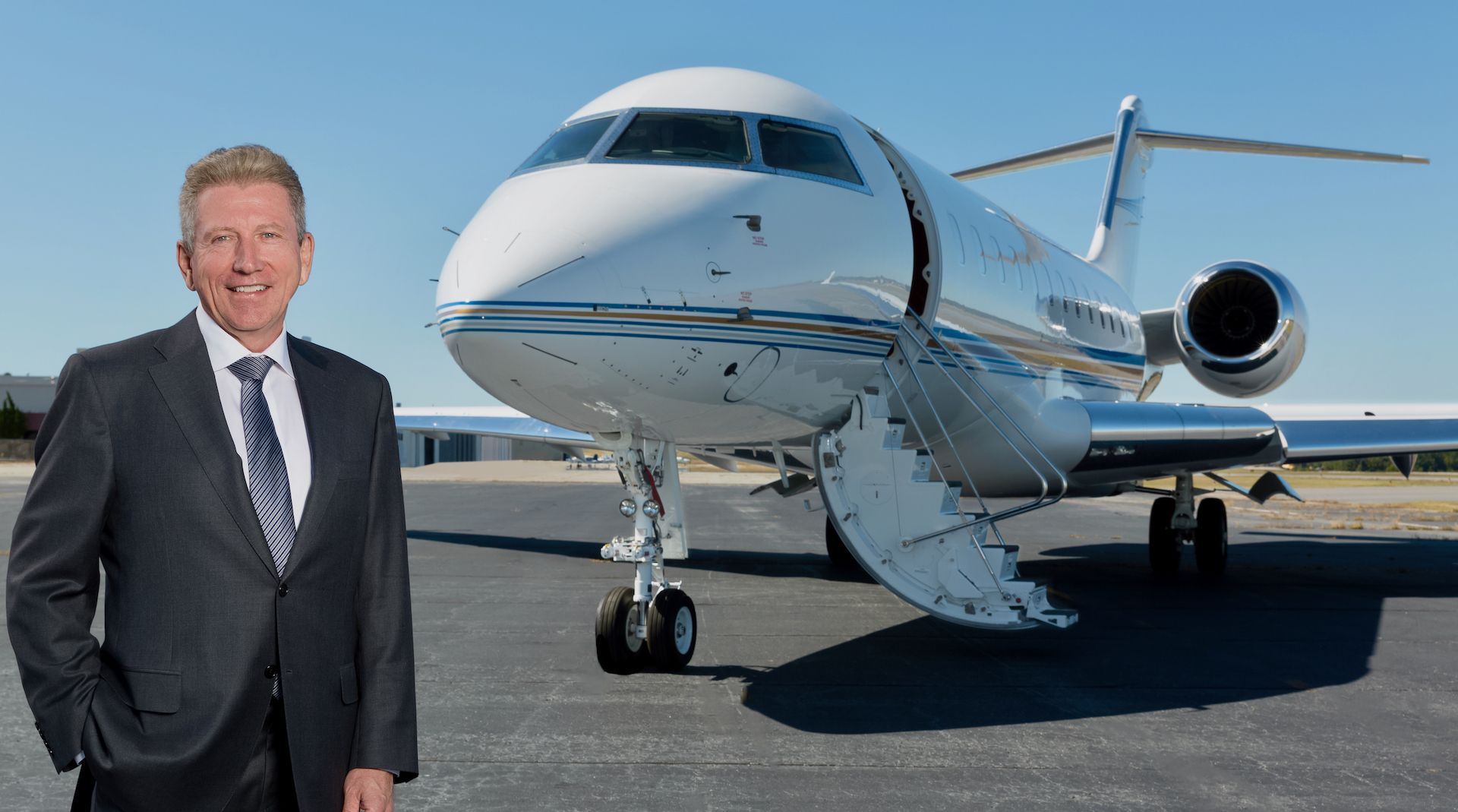 Scott Rogers at Amjet Aviation; Man in suit stands beside a private jet on a tarmac.