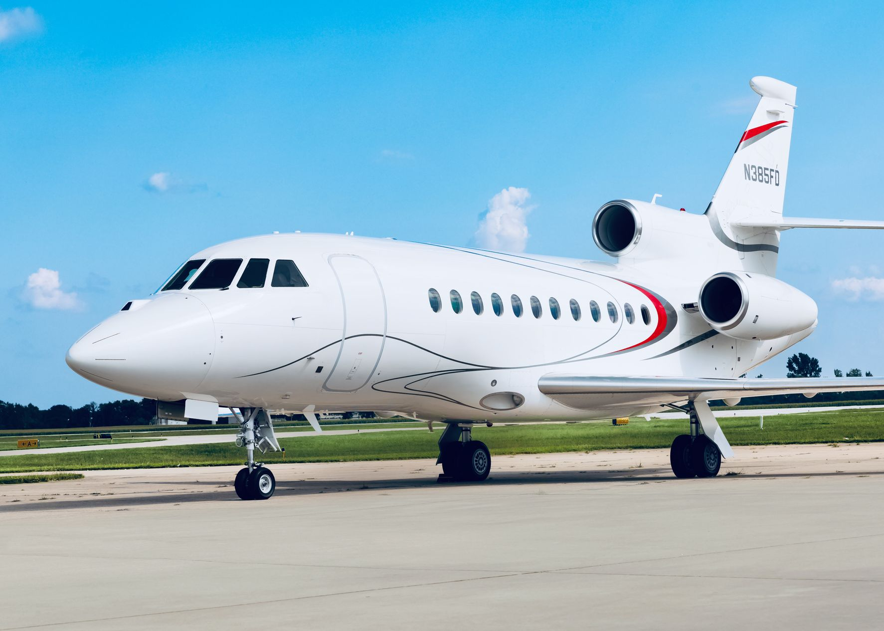 White Dassault Falcon 900EXy private jet on a tarmac, red and black accents, under a blue sky.