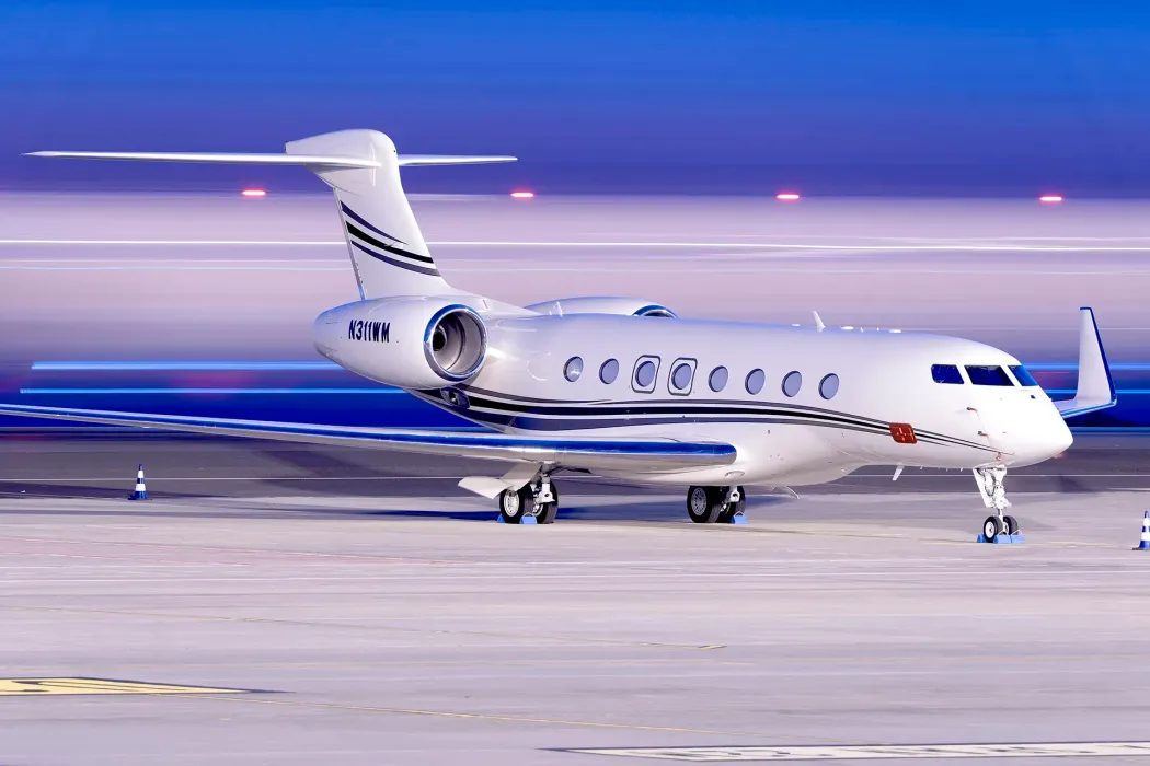 A white Gulfstream private jet parked on an airport tarmac at dusk under a blue and pink gradient sky.