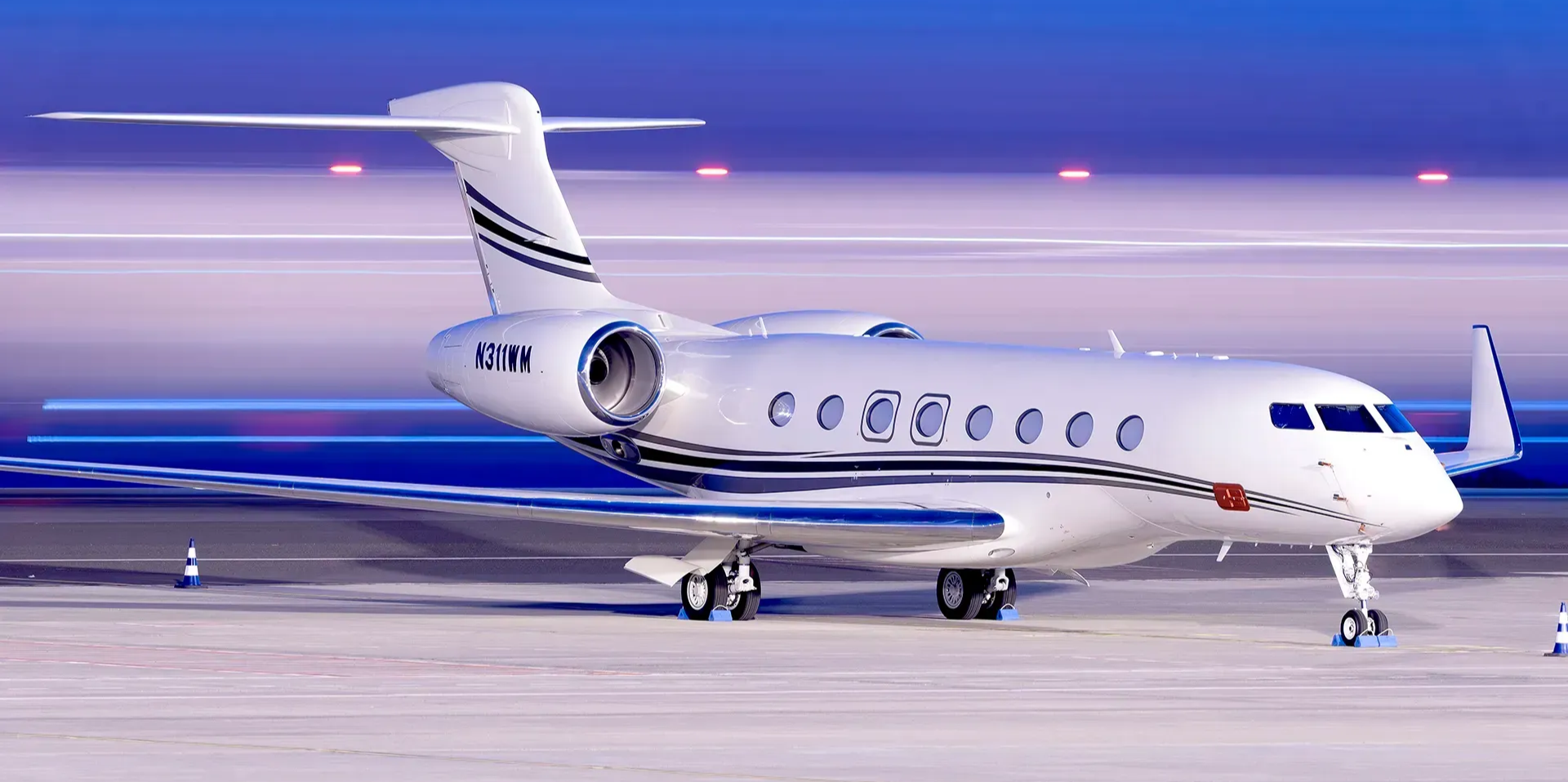 A white Gulfstream private jet parked on an airport tarmac at dusk under a blue and pink gradient sky.