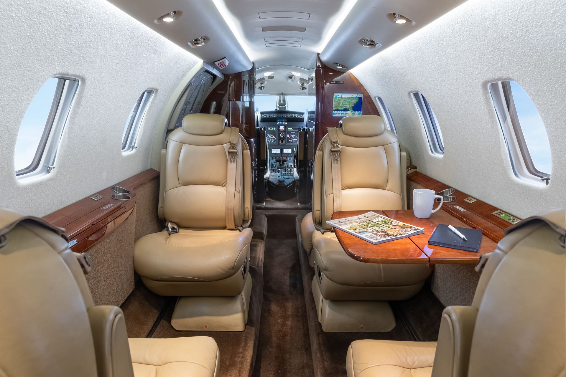 Interior of a private jet with tan leather seating, wood paneling, and a small table.