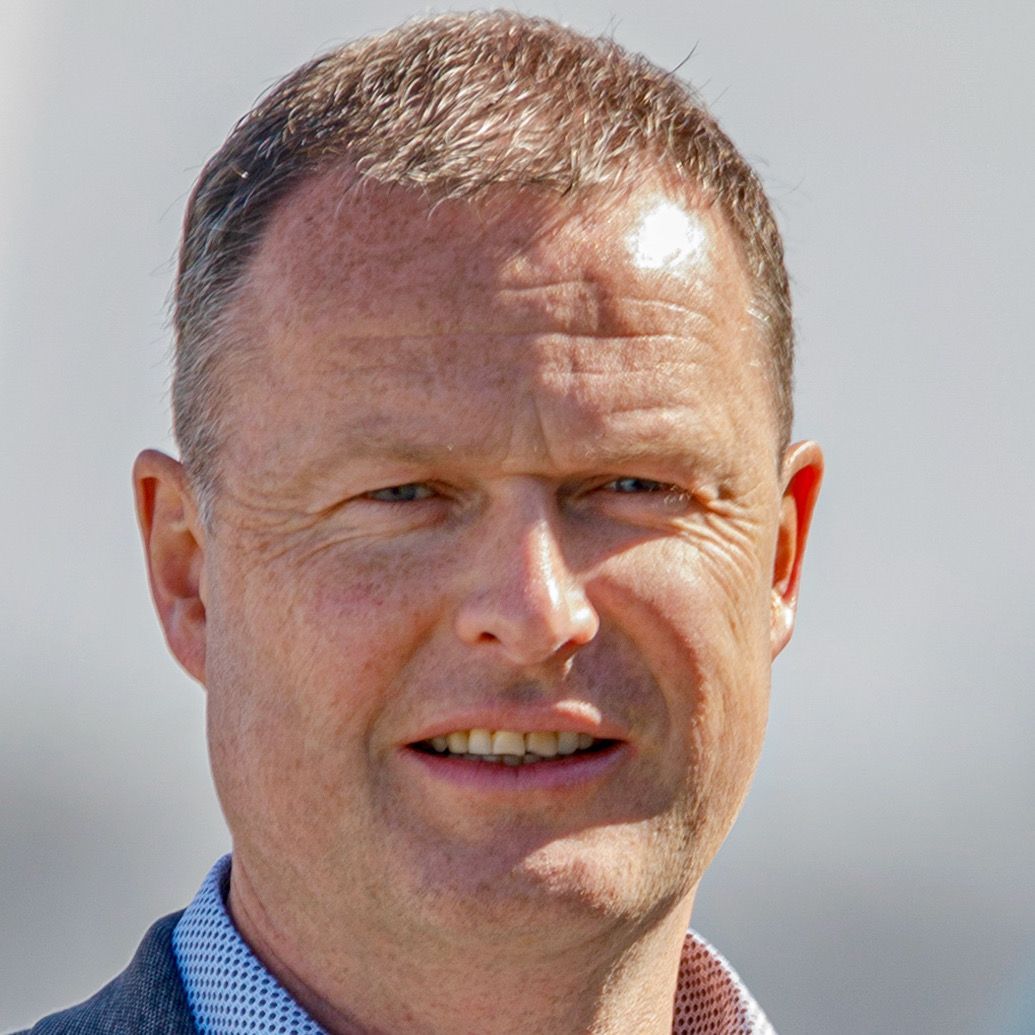 Lutz Druschke at Amjet Aviation; Man with short brown hair smiles, wearing a patterned blue shirt and grey jacket, outside.