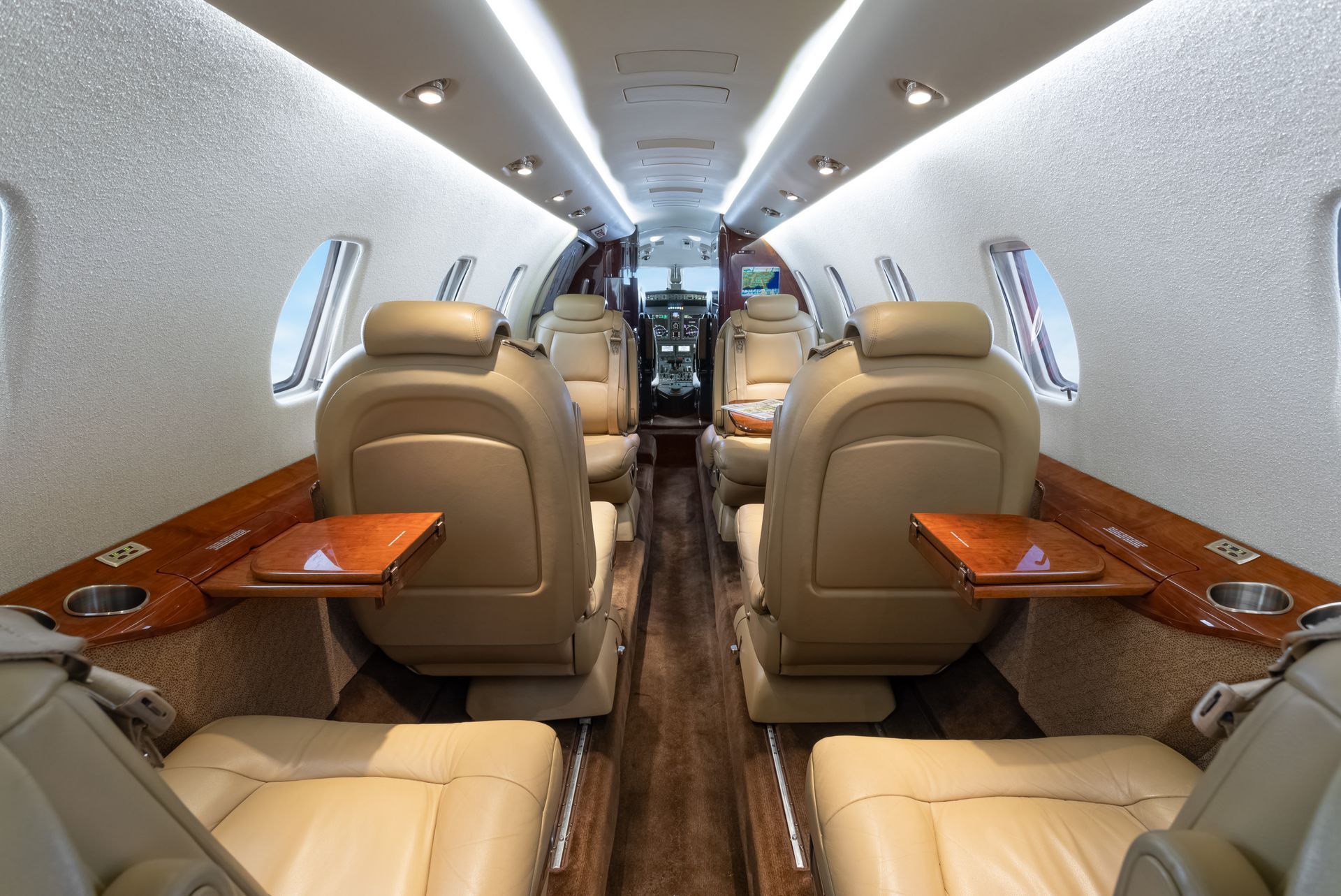 Interior of a private jet with beige leather seats, wooden tables, and overhead lighting.