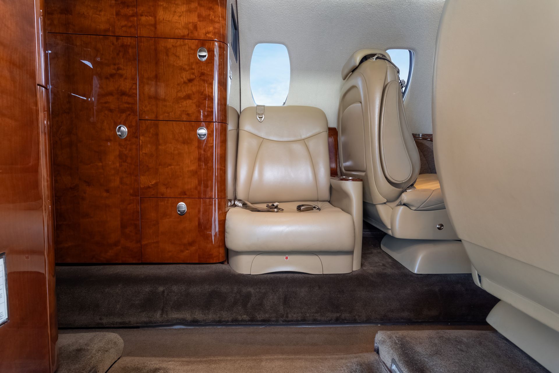 Interior of a private jet with beige leather seats, dark wood paneling, and a brown carpet.