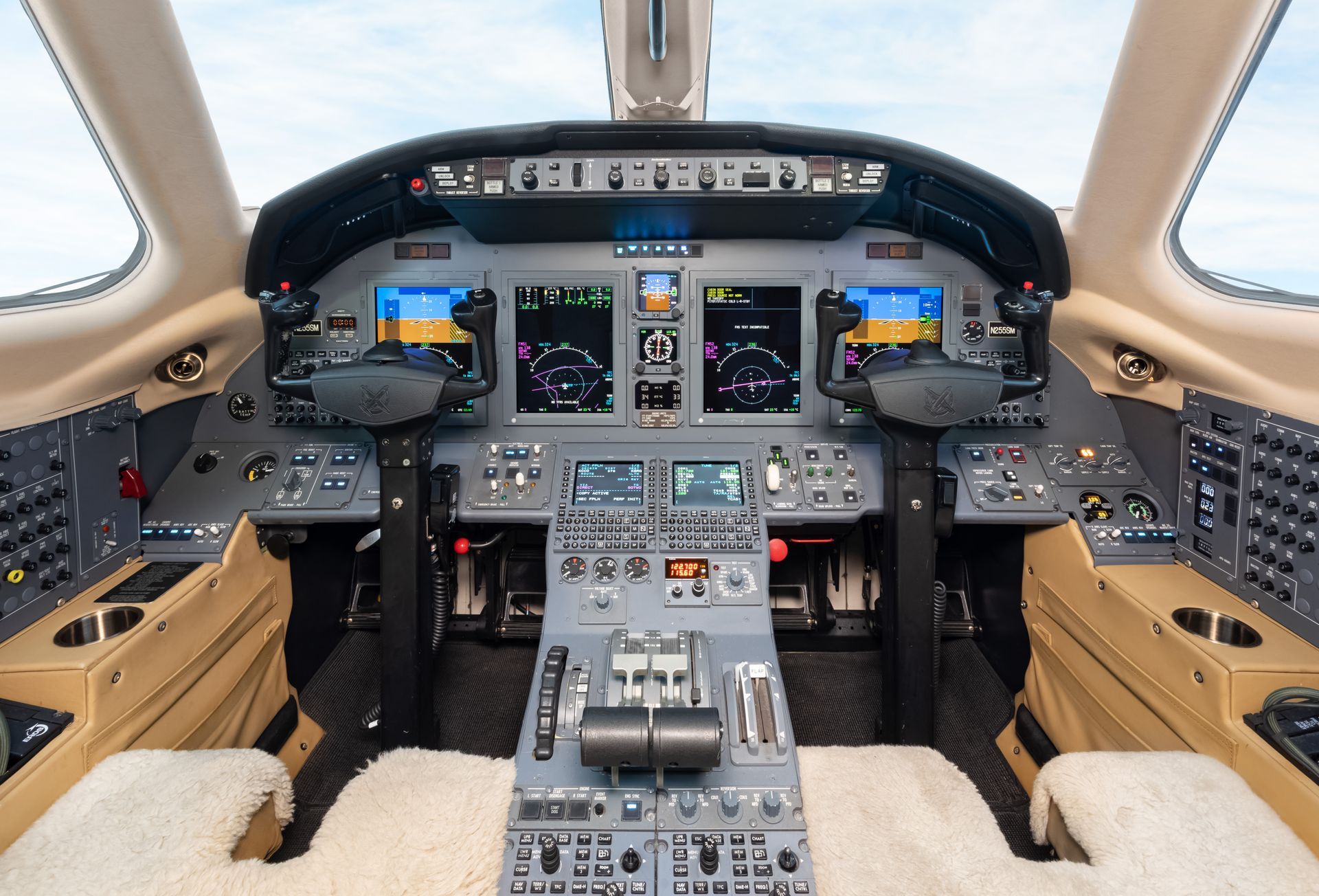 Cockpit of a private jet, filled with instrument panels and controls, tan interior, clear sky visible.