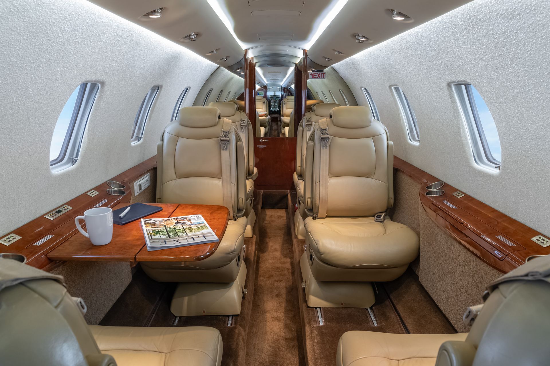 Interior of a private jet with tan leather seating and a small wooden table.