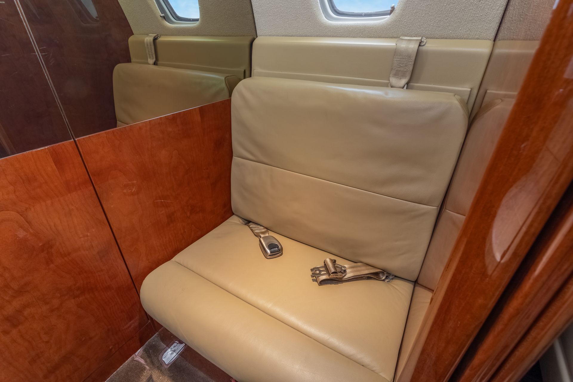 Beige leather airplane seat with a seatbelt, wood paneling.