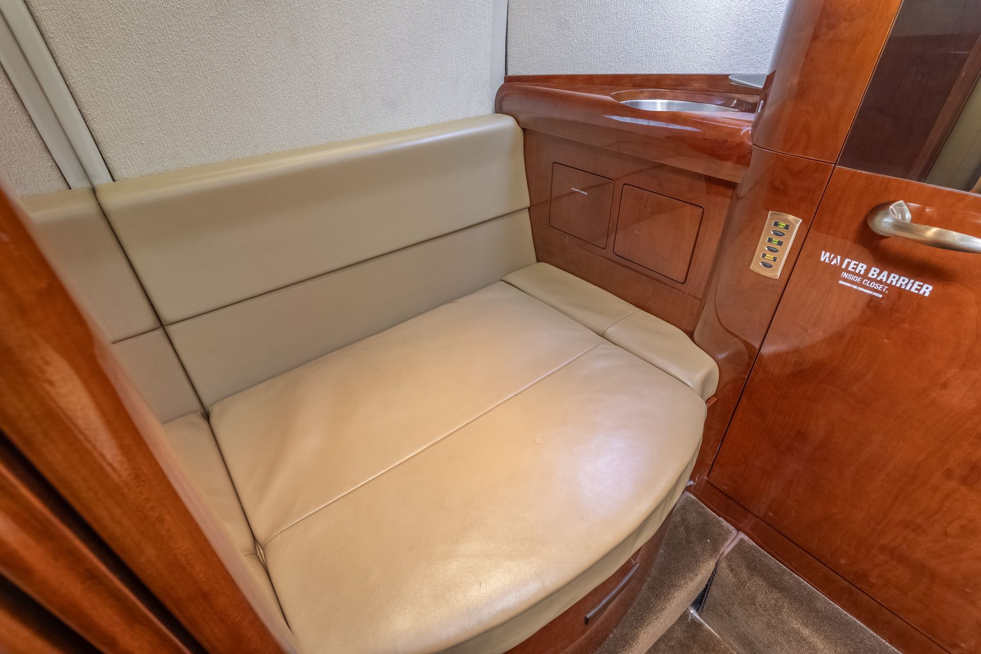 Small airplane lavatory with tan seat, wood paneling, and a door.