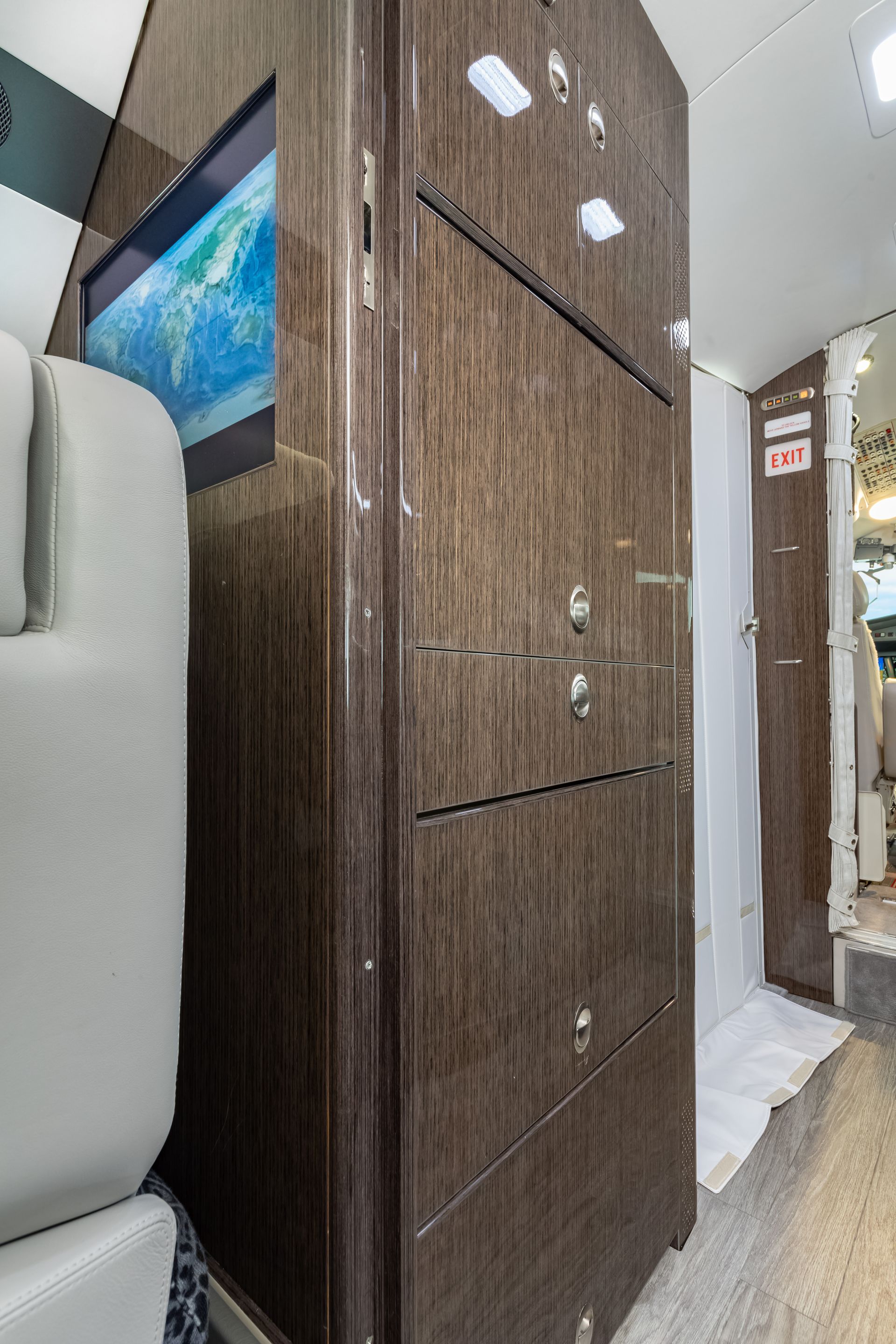 A wood-paneled cabinet in a plane, with a TV screen displaying a world map and gray seating.