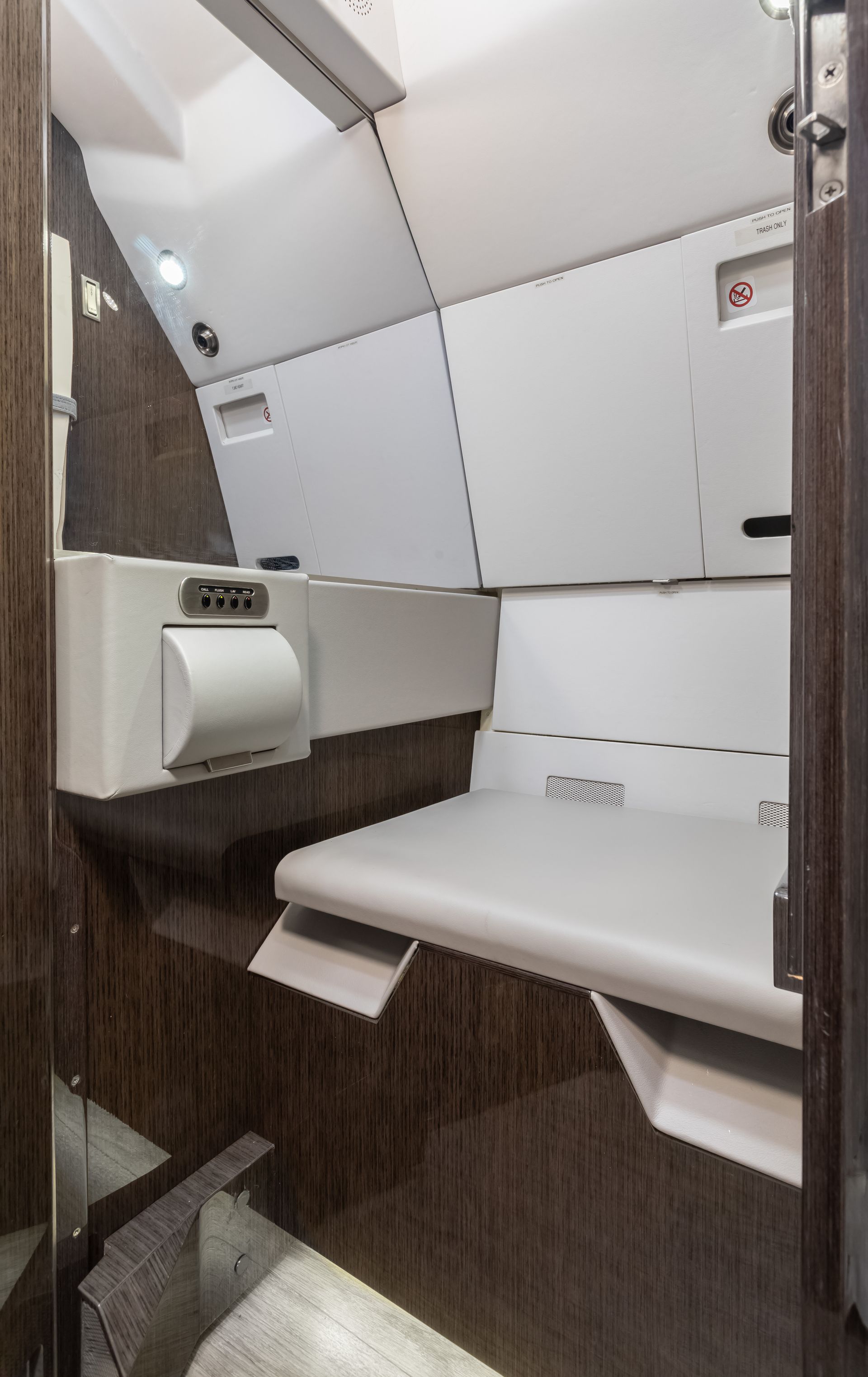 Airplane lavatory with changing table. White changing table, toilet paper dispenser, and cabinetry, brown wood paneling.