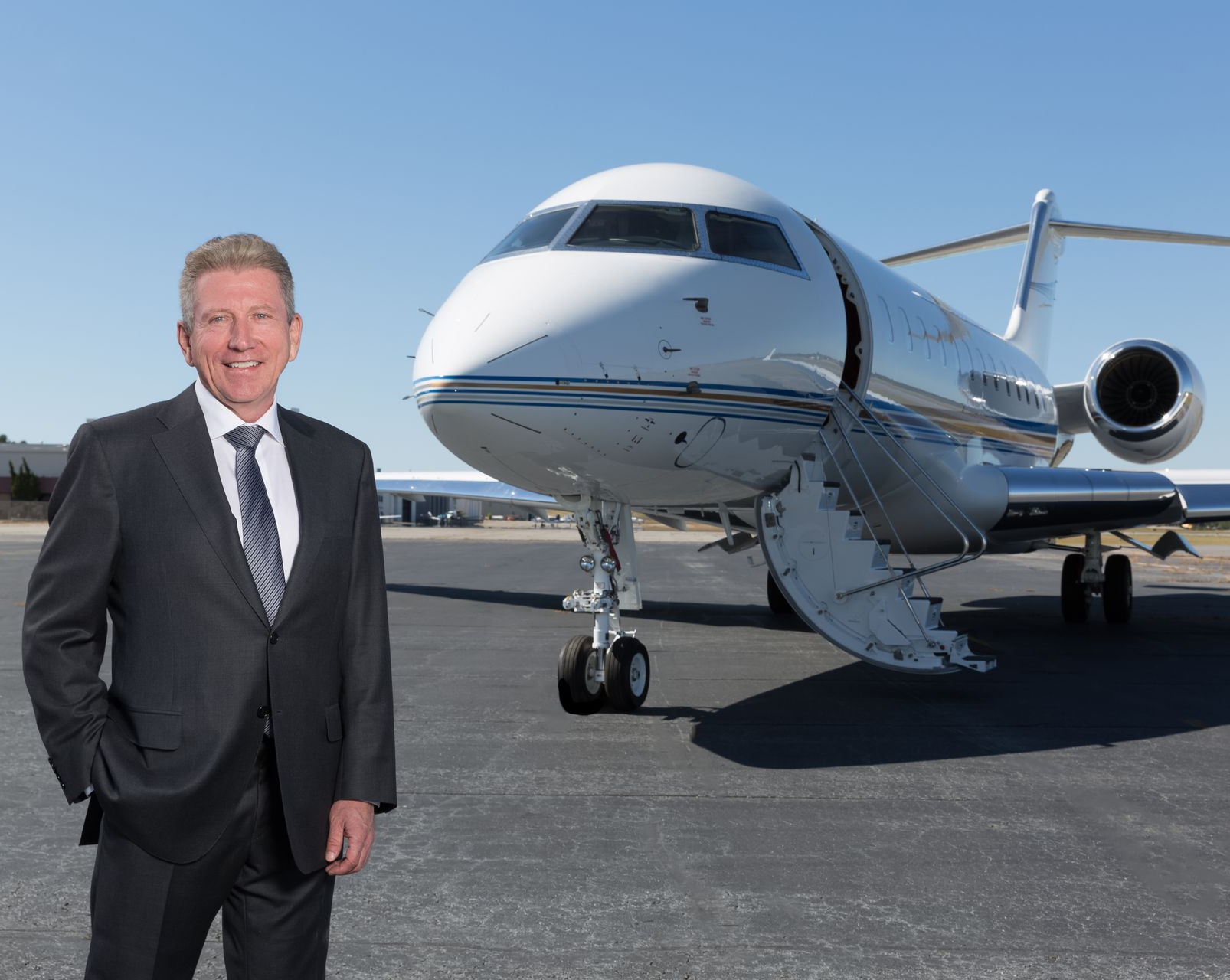 Scott Rogers at Amjet Aviation; Man in suit stands beside a private jet on a tarmac.