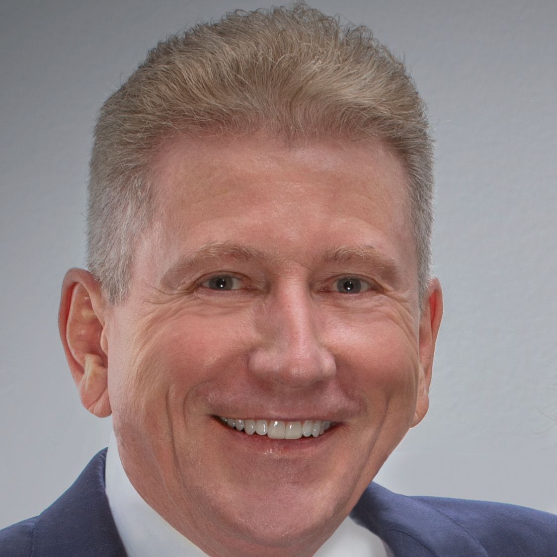 Scott Rogers at Amjet Aviation; Man with light skin smiling, wearing a blue suit, against a gray background.