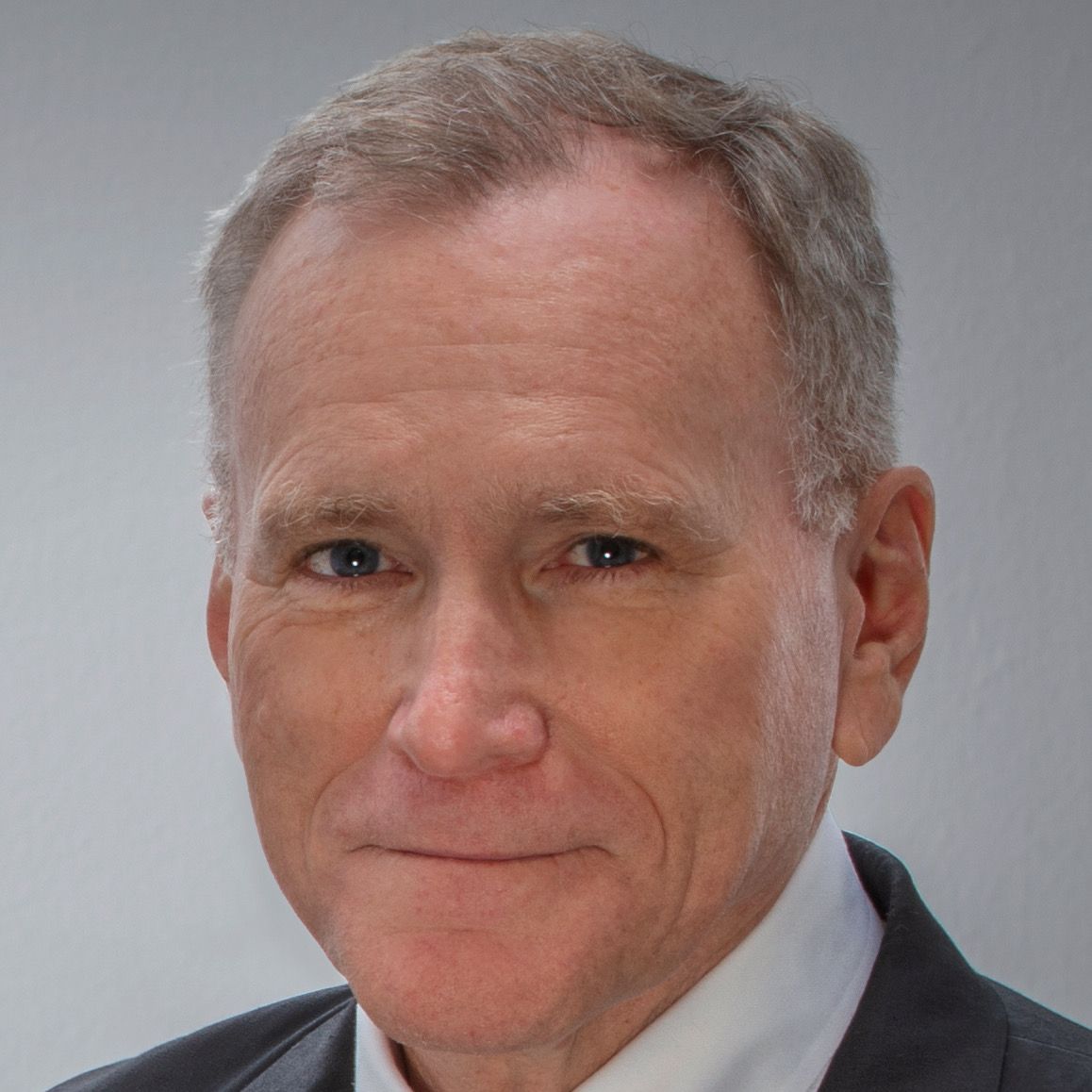 Tom Rogers at Amjet Aviation; Man in a suit smiles at the camera, indoors, neutral background.