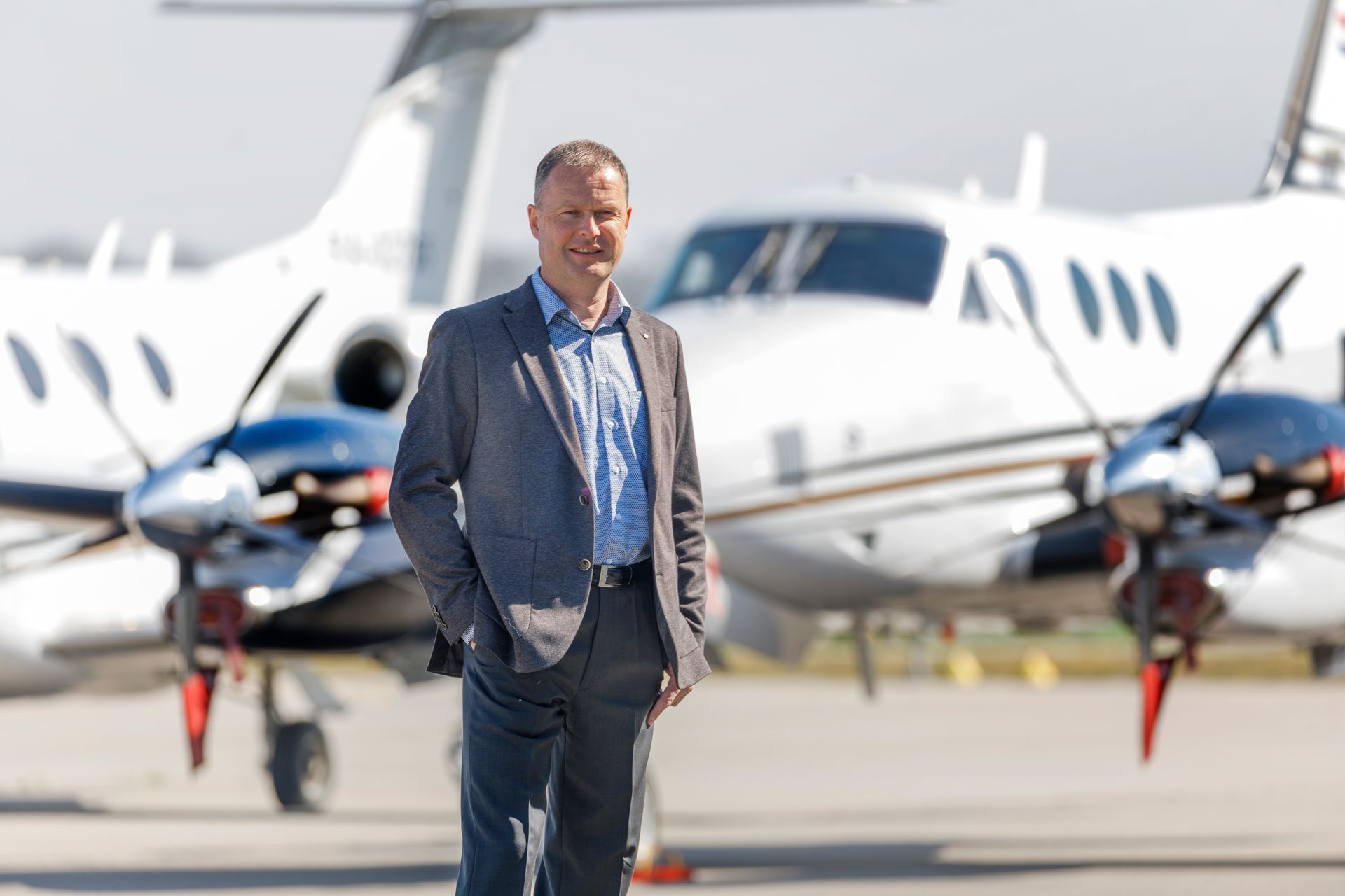 Lutz-Philip Druschke; Man in suit stands in front of a white airplane on a sunny tarmac.