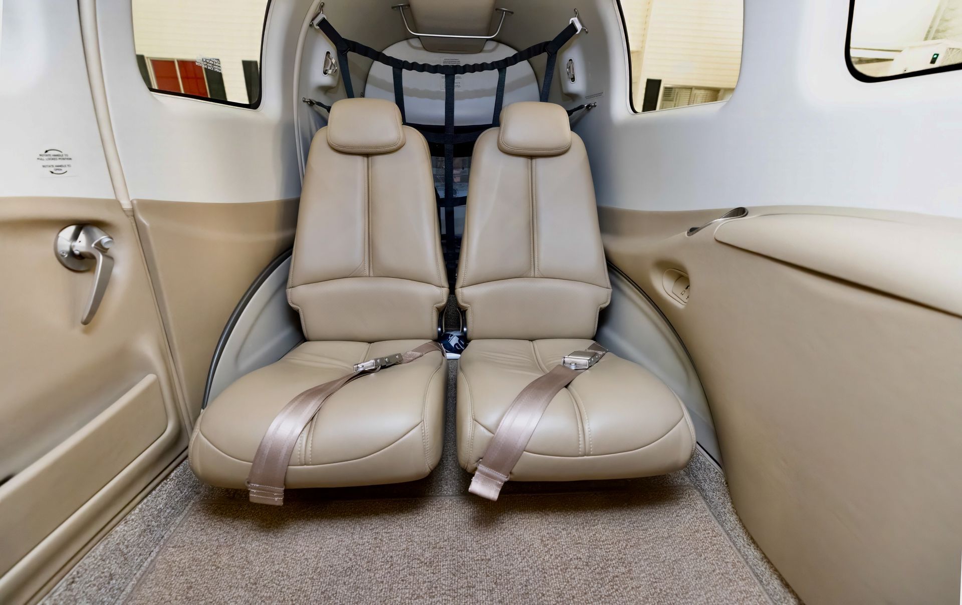 Interior of an aircraft cabin with two tan leather seats, beige walls, and a light brown carpet.
