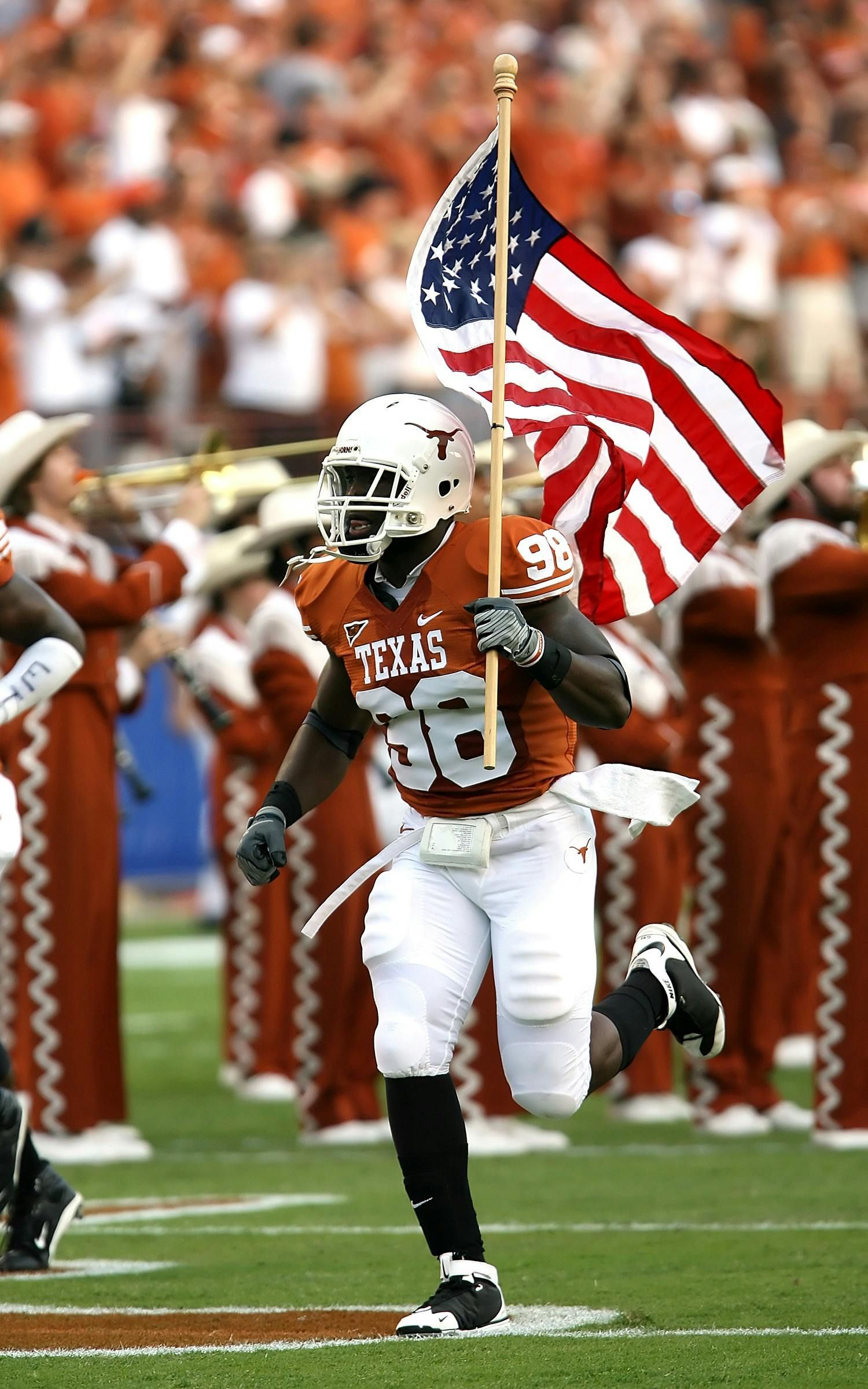 Football player in Texas uniform runs with American flag, stadium in background.
