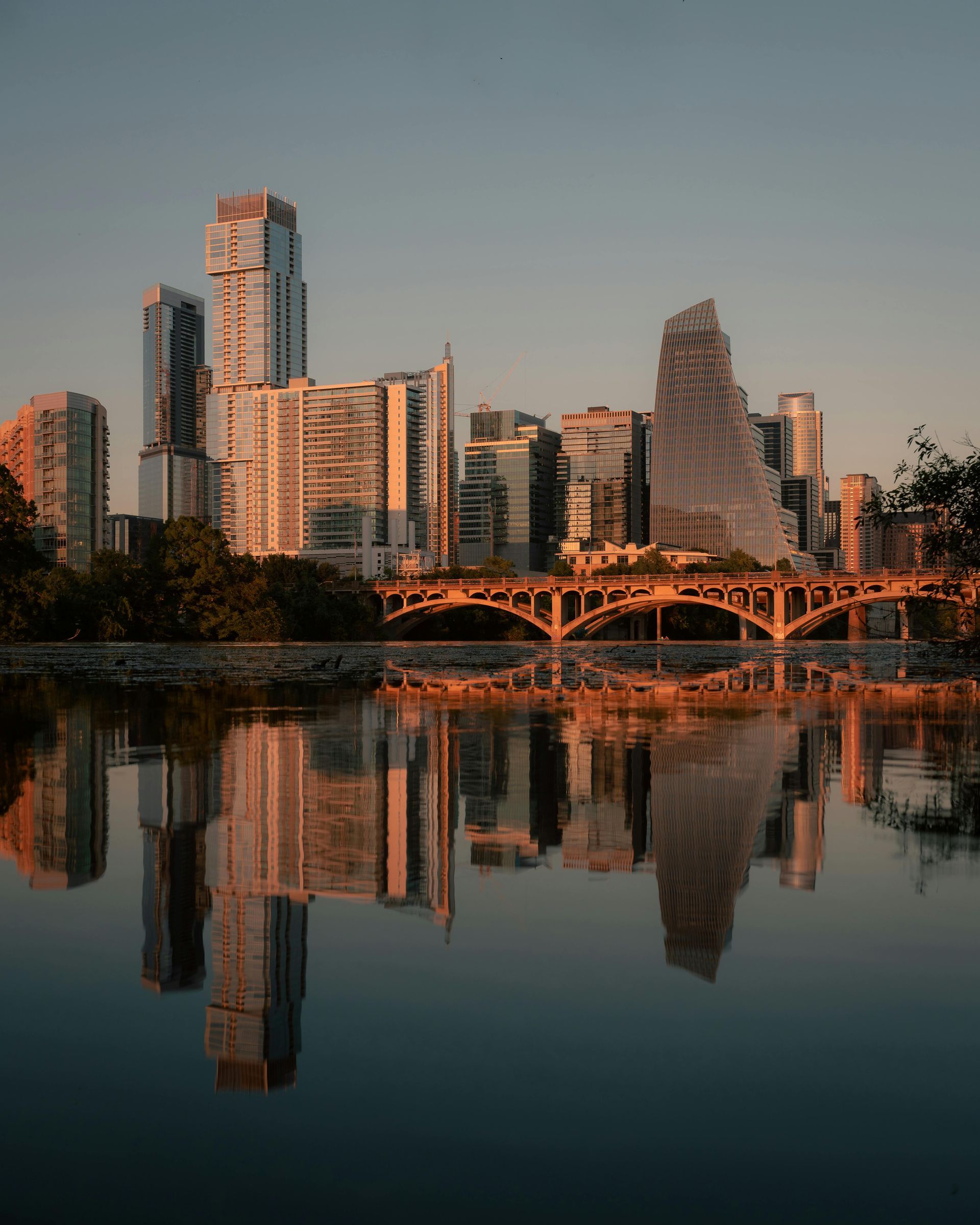 Austin, Texas skyline at sunset, reflected in the water, with gold and orange hues.