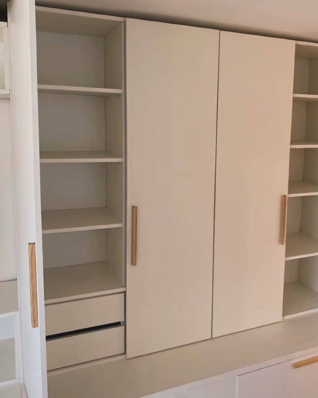 Mueble de almacenaje empotrado de color blanco con estantes abiertos, dos puertas y tiradores en tono madera.