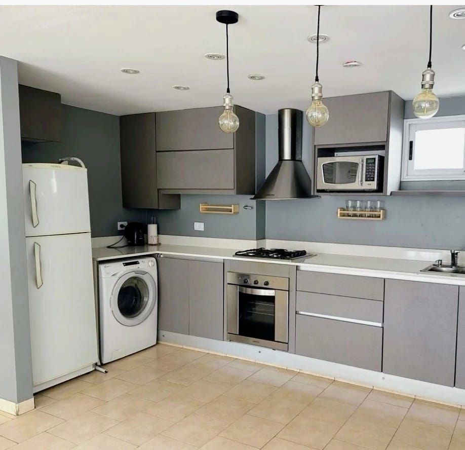 Cocina gris con electrodomésticos: refrigerador, lavadora, estufa, microondas y campana extractora.