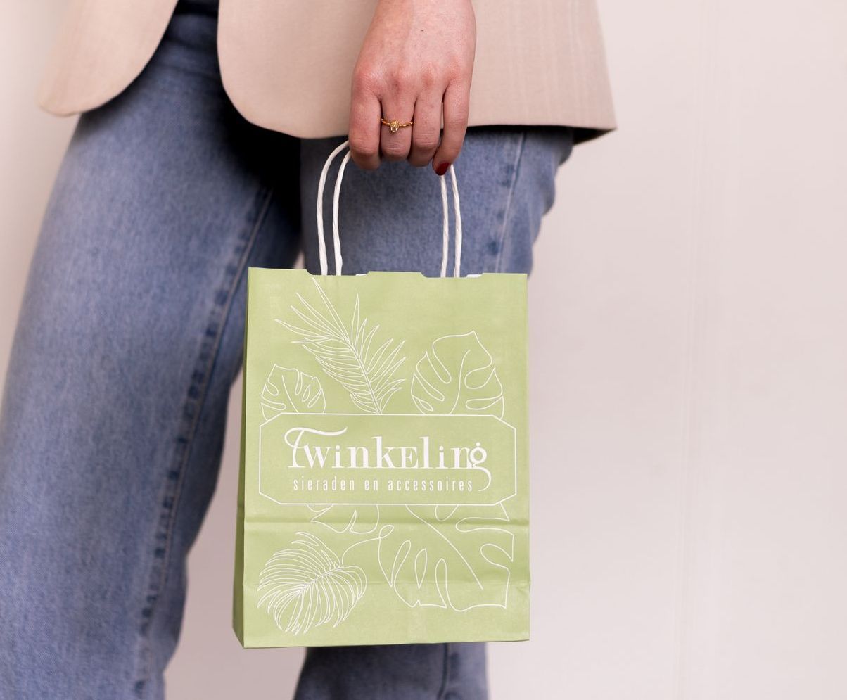 Een vrouw houdt een groene papieren tas vast met het woord winkeling erop.