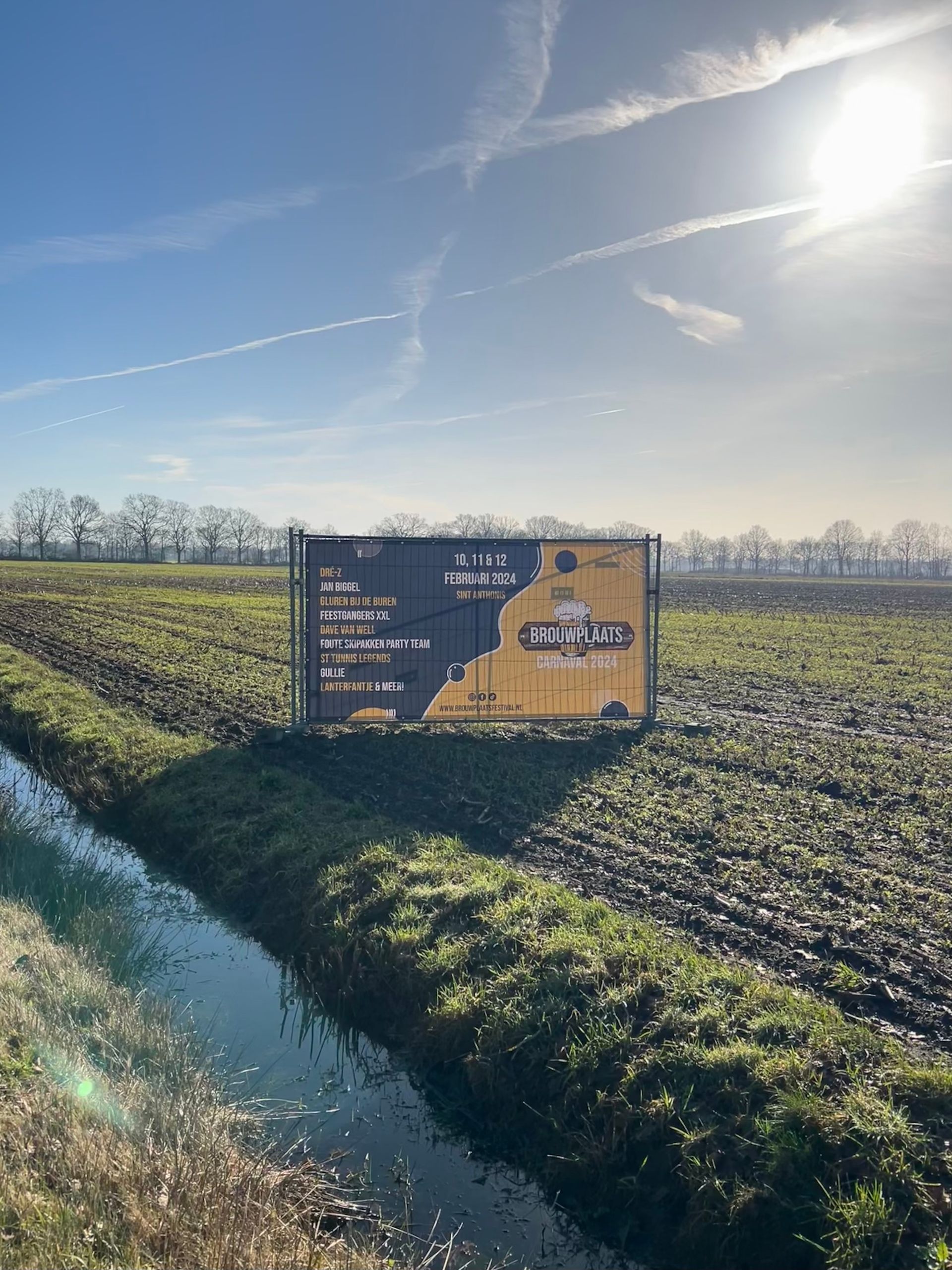 Een groot reclamebord staat midden in een veld naast een rivier.