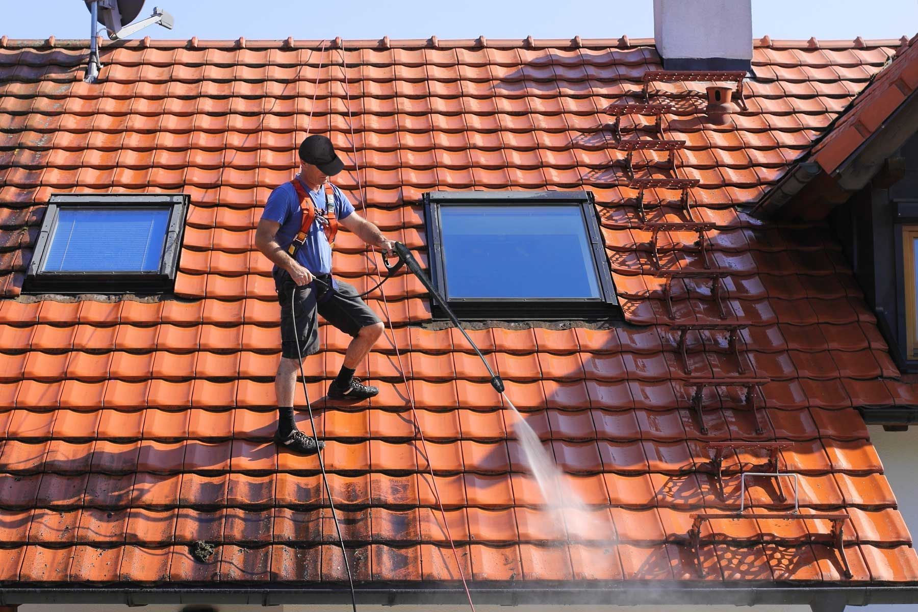 A man is cleaning the roof of a house with a high pressure washer.