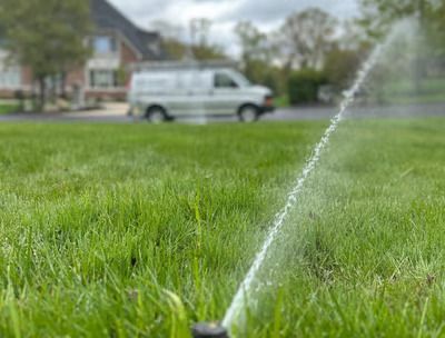 A sprinkler is spraying water on a lush green lawn with a van in the background.