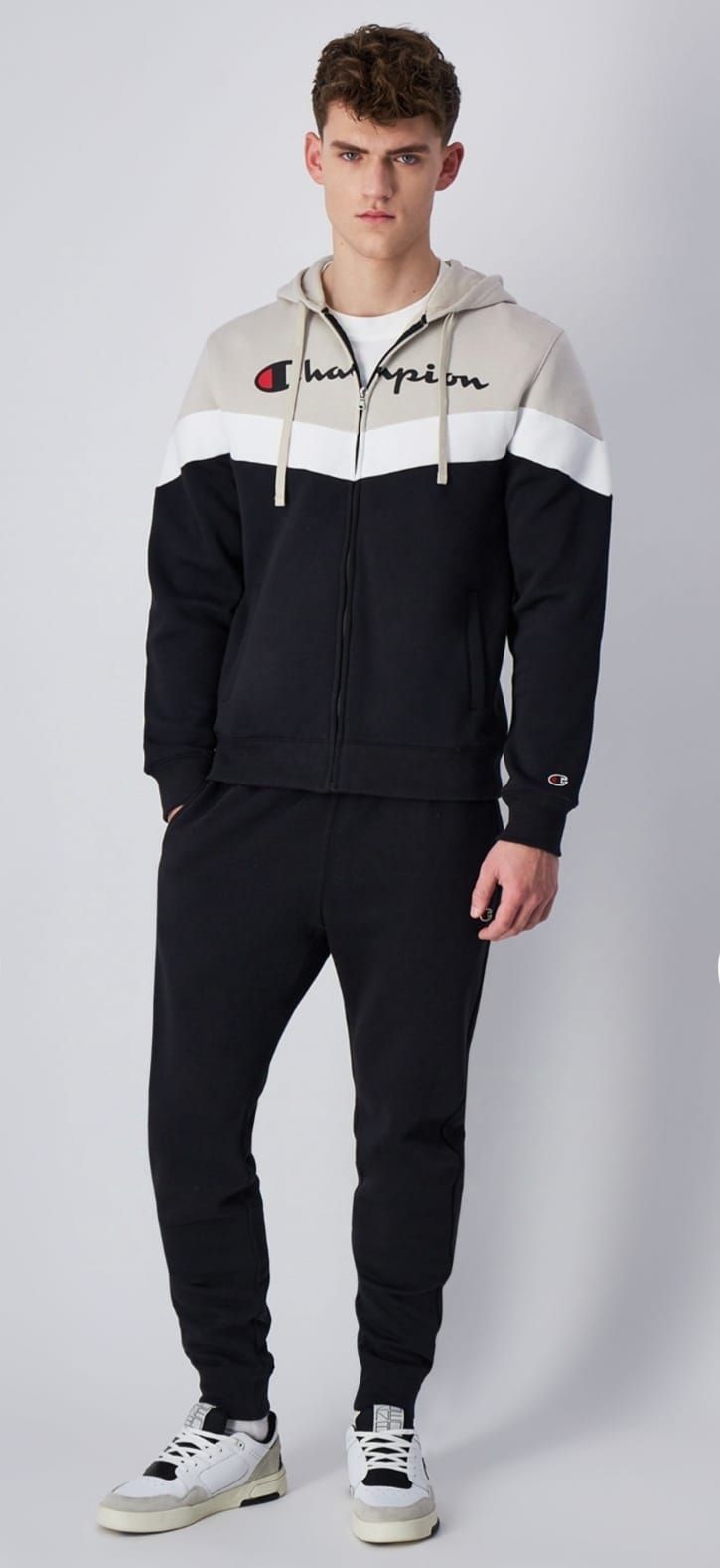 Un uomo indossa una felpa con cappuccio bianca e nera della Champion e pantaloni della tuta neri.