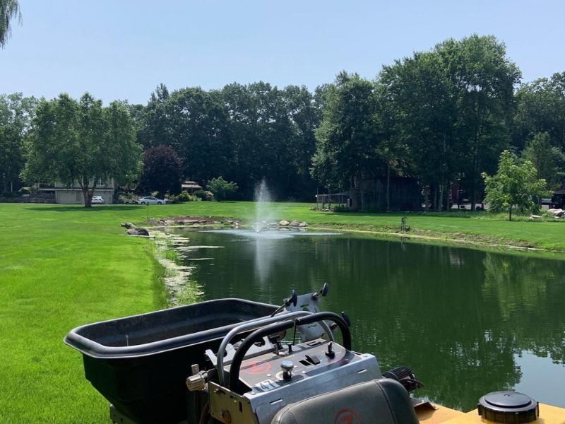 A lawn mower is parked next to a pond with a fountain in the background.