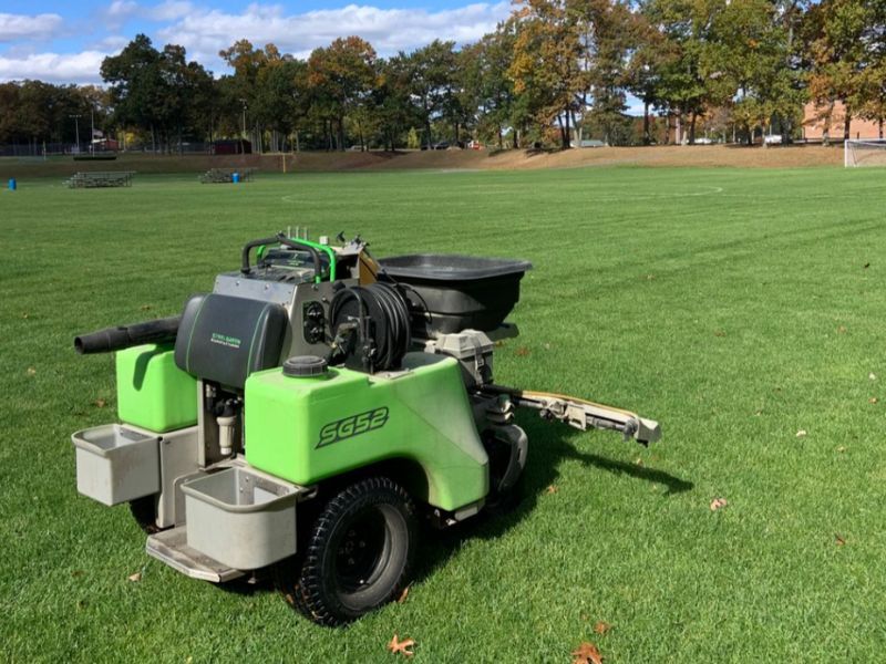 A green lawn mower is sitting on top of a lush green field.