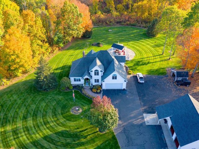 An aerial view of a large house with a lush green lawn surrounded by trees.